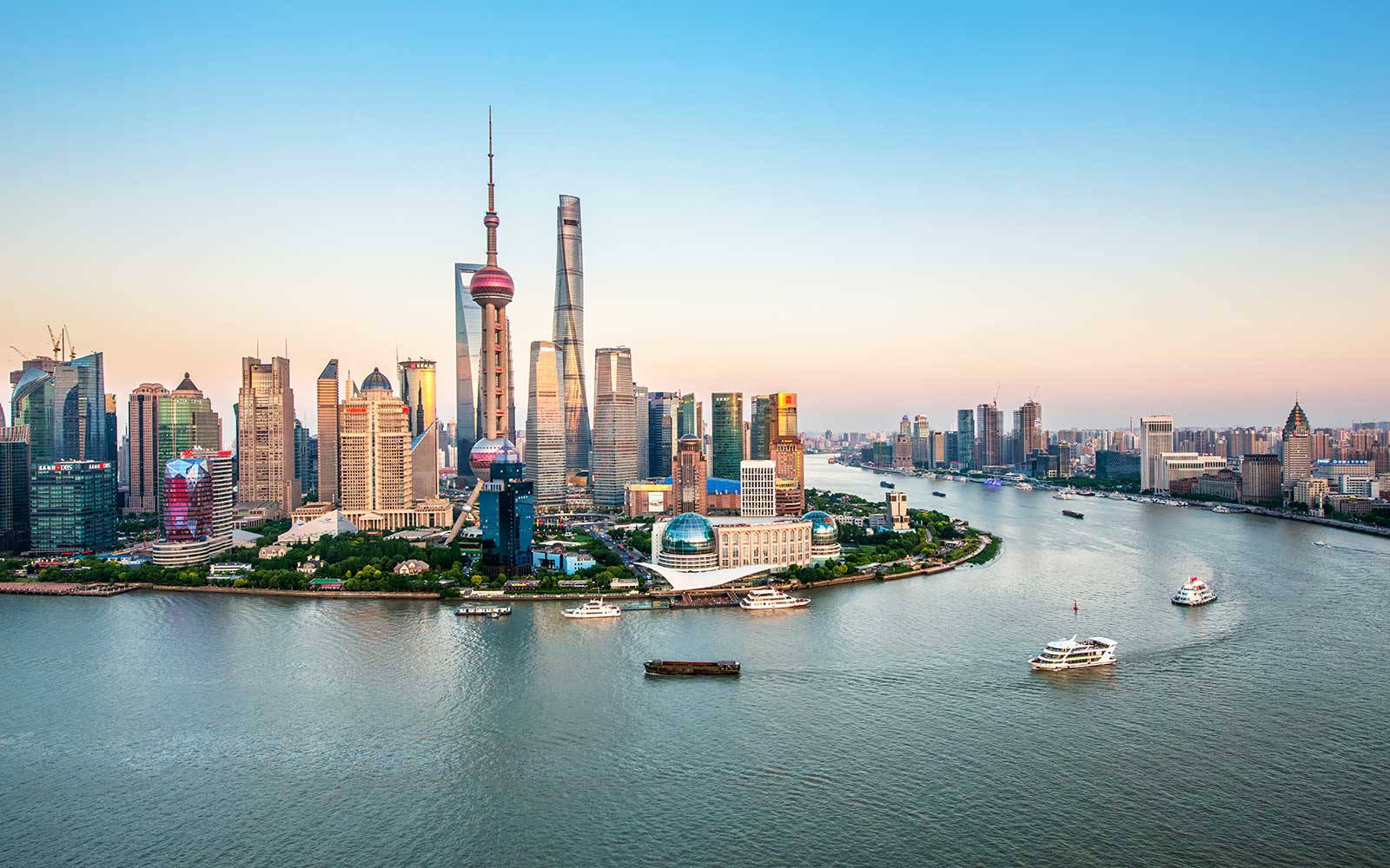 Asia 桌布 壁紙 — 夕陽將上海標誌性的天際線和黃浦江沐浴在溫暖的金色光芒中，船隻在水面上滑行。