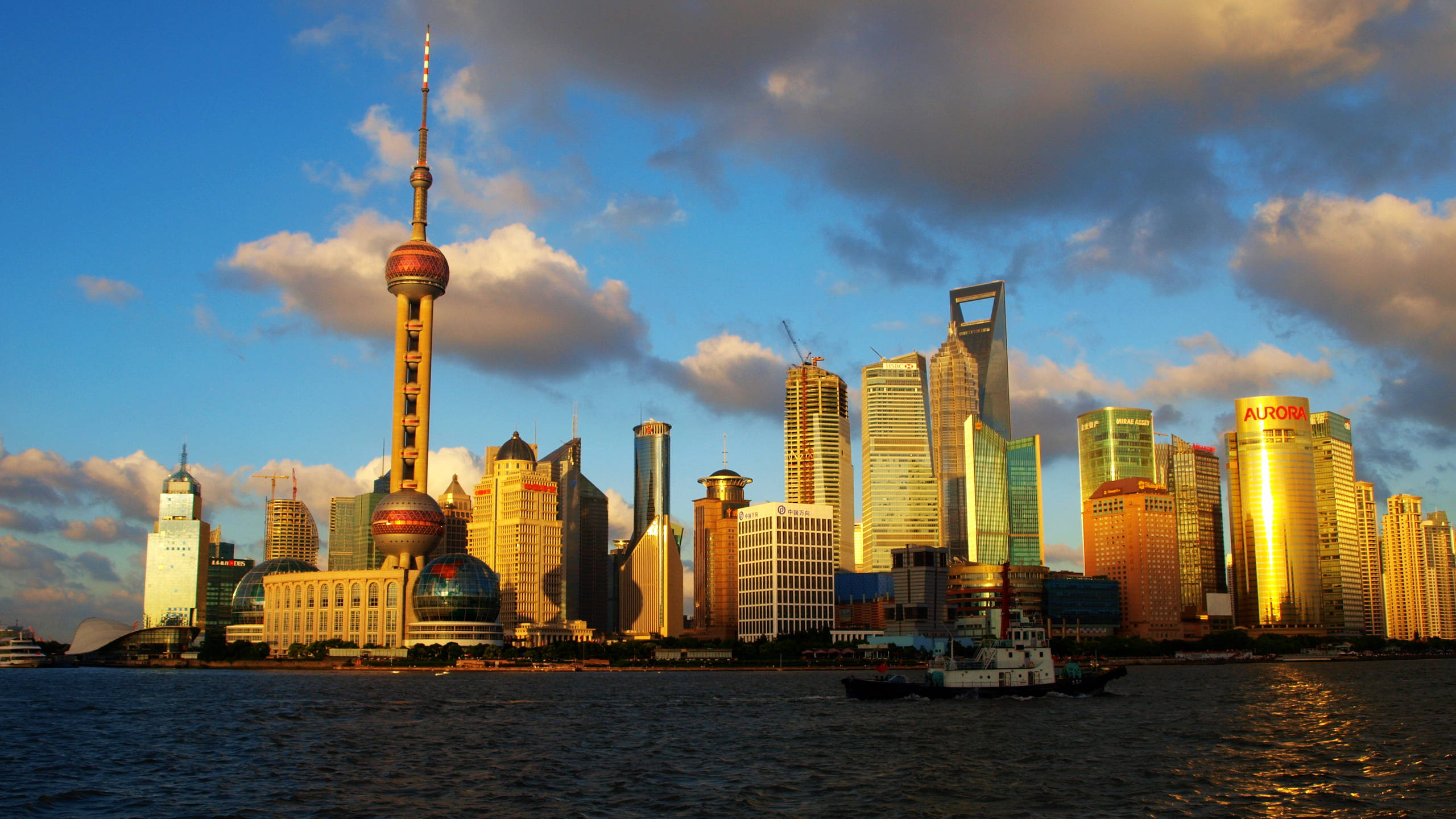 Shanghai 桌布 壁紙 — 夕陽將上海標誌性的天際線沐浴在金色光芒中，現代摩天大樓倒映在下面的黃浦江上。