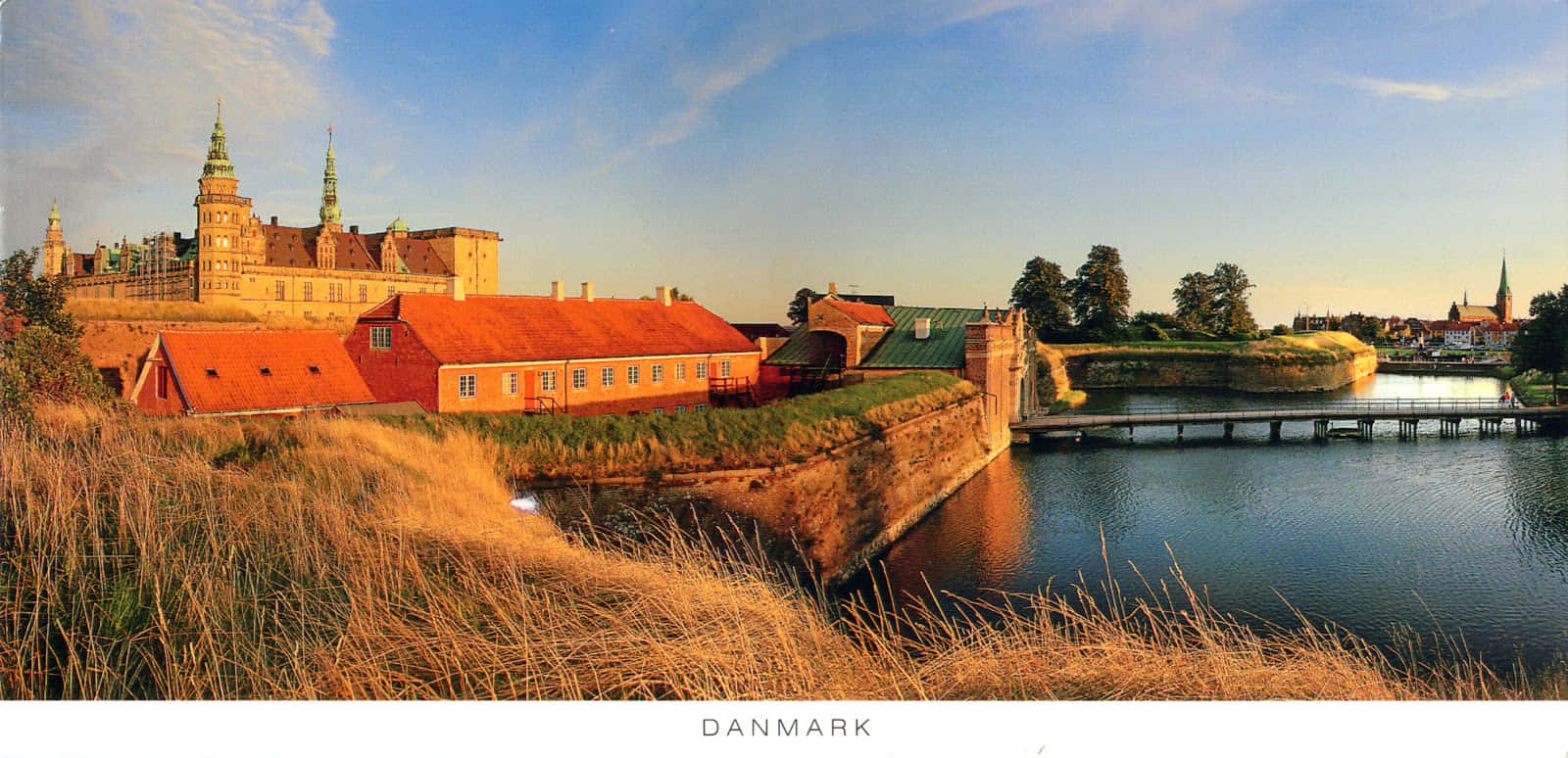 Denmark 桌布 壁紙 — 夕陽將丹麥城堡和紅頂建築沐浴在金色光芒中，倒映在平靜的水面上。