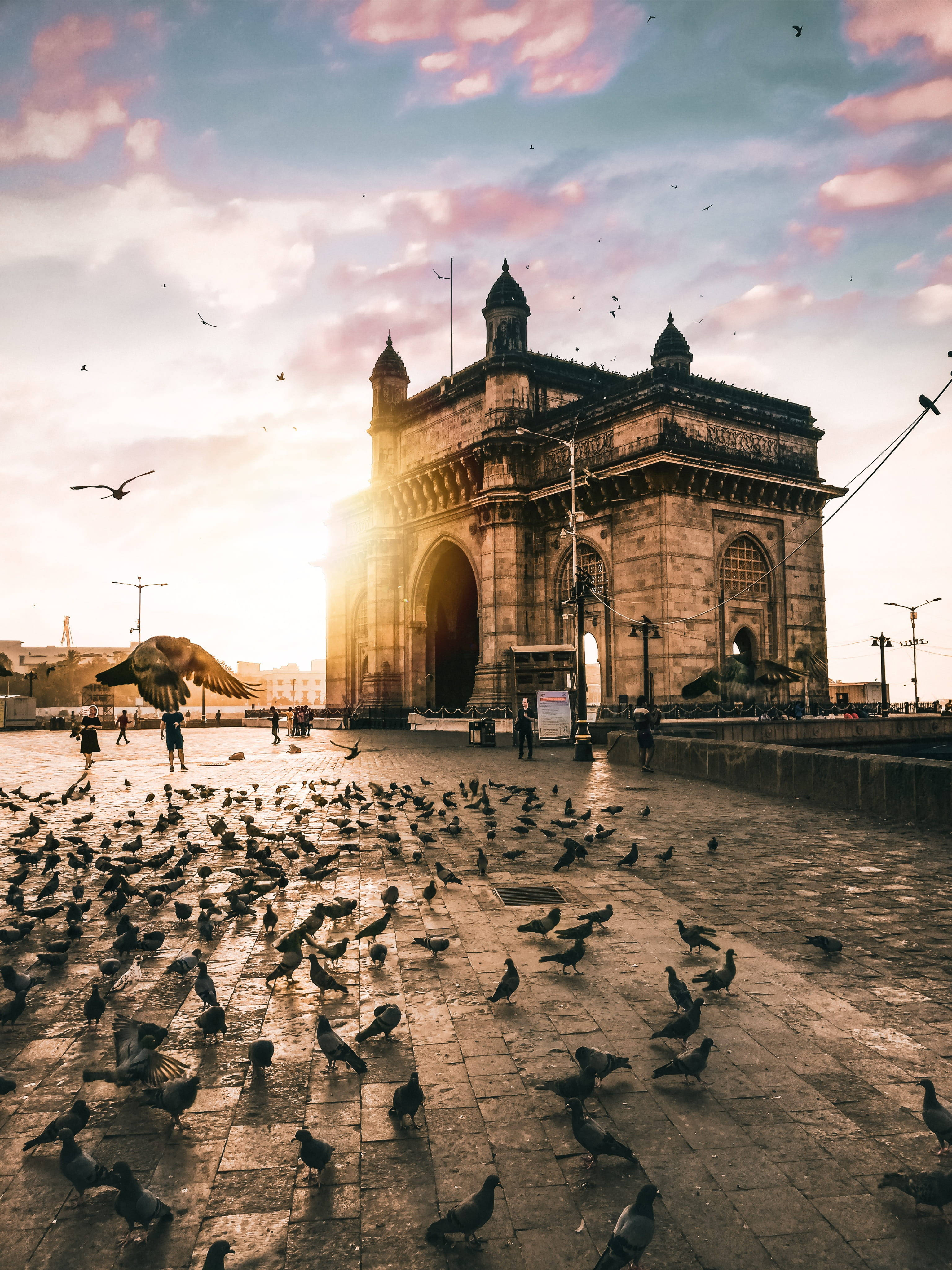 Mumbai 桌布 壁紙 — 夕陽將印度門沐浴在金黃色的光芒中，鴿子在下面的廣場上散開。