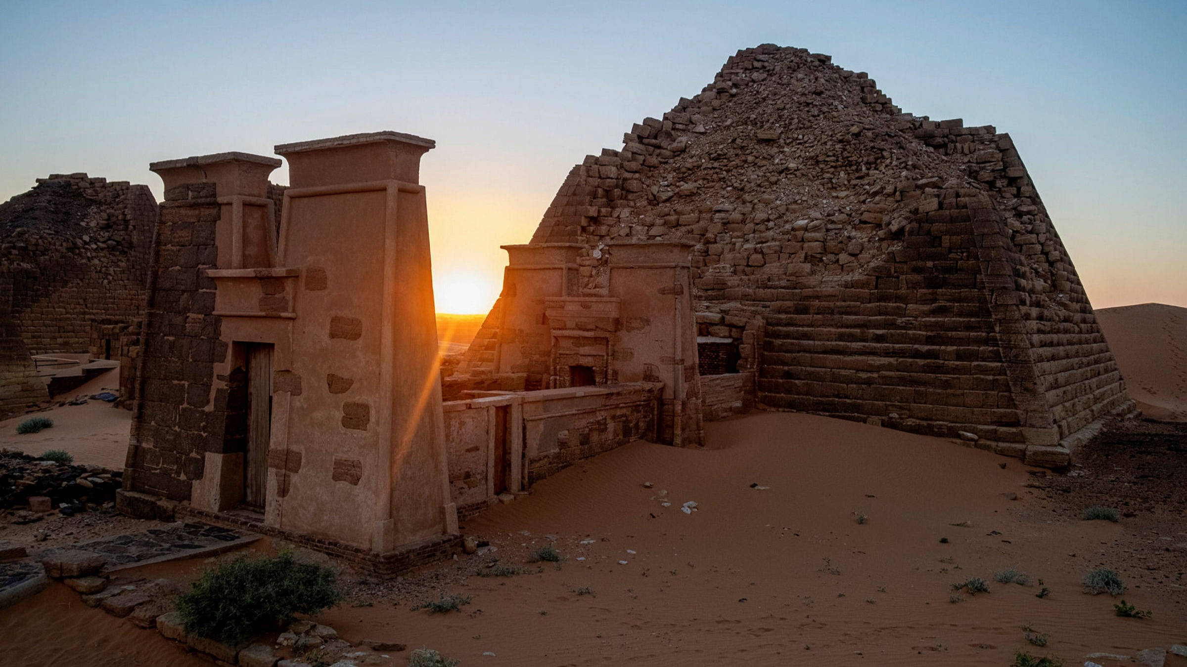 Sudan 桌布 壁紙 — 夕陽將古埃及階梯金字塔和石頭廢墟沐浴在溫暖的金色光芒中，映襯著沙漠天空。