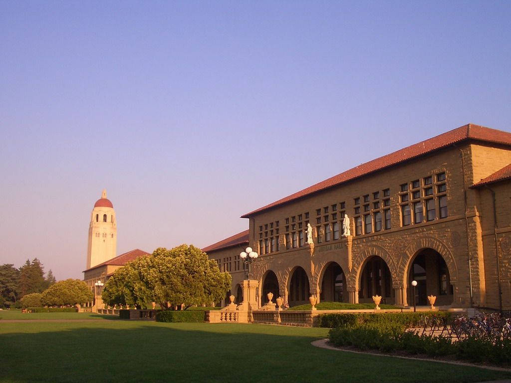 樹木 桌布 壁紙 — 夕陽將史丹佛大學標誌性的砂岩建築和鐘樓沐浴在溫暖的金色光芒中，照耀在修剪整齊的草坪上。