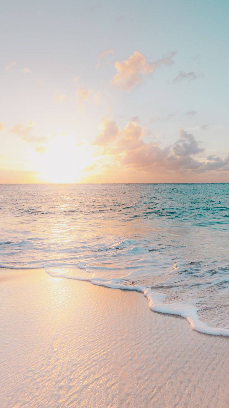 iPhone X Beach 桌布 壁紙 — 夕陽將天空和海洋染成柔和的蜜桃色和金色，溫柔的海浪輕吻著沙灘。