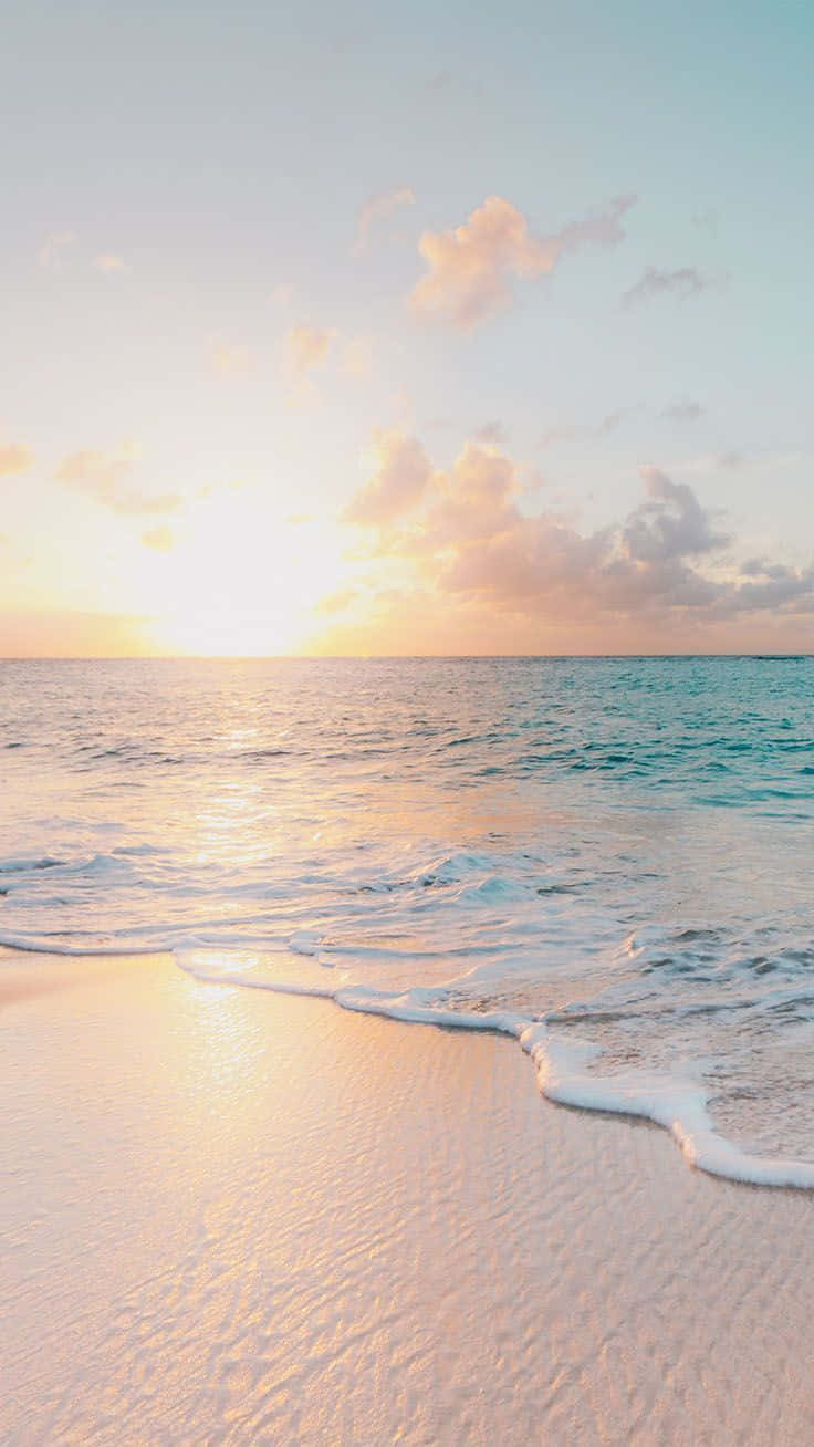 Pastel Beach 桌布 壁紙 — 夕陽將天空和海洋染成溫暖的金色和粉紅色，溫柔的海浪輕撫著柔軟的沙灘。