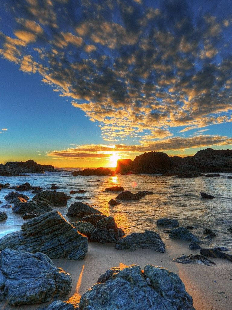 自然風景動圖 桌布 壁紙 — 夕陽將天空和海洋染成金色，光線在崎嶇海岸線的濕岩石上閃爍。