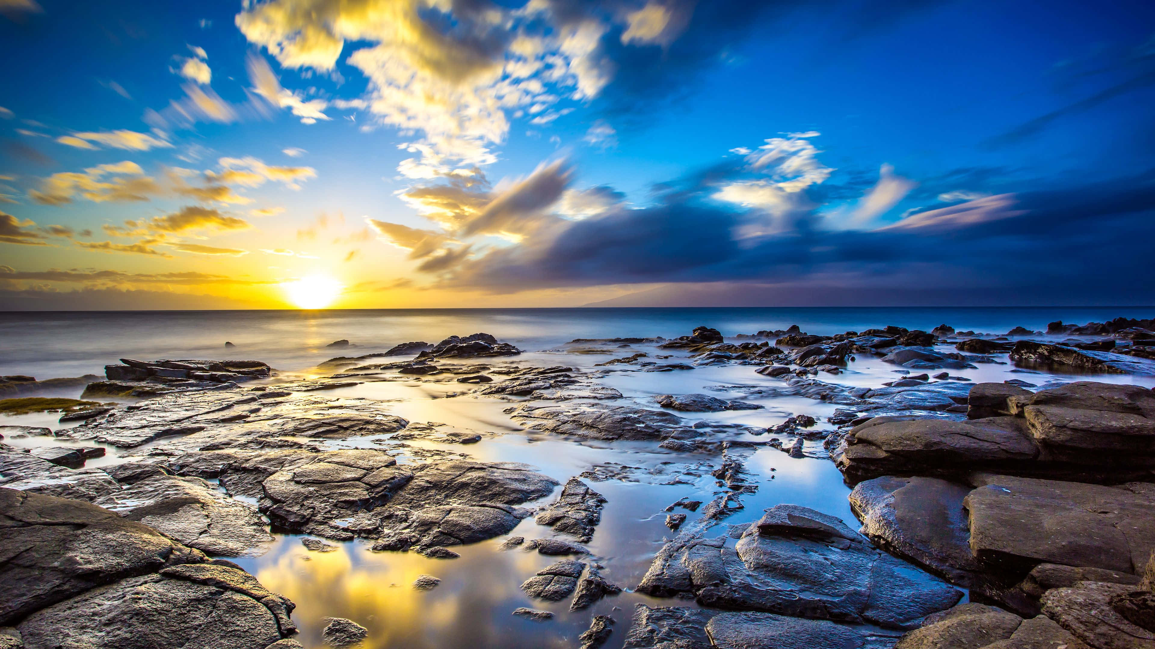 Rocks 桌布 壁紙 — 夕陽將天空和海洋染成金藍色，海浪輕輕拍打著紋理豐富的沿海岩石。