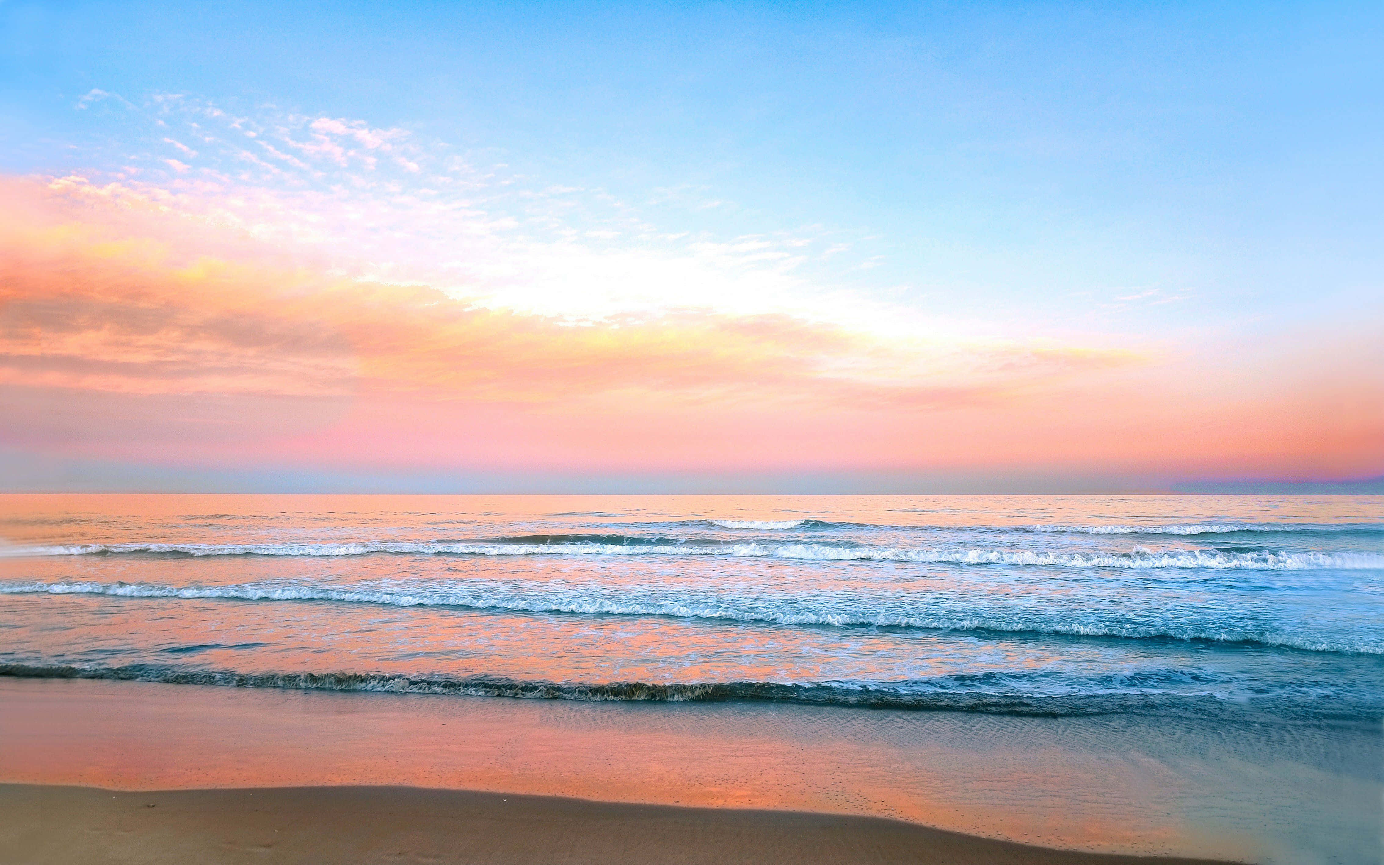 Pastel Beach 桌布 壁紙 — 夕陽將天空染成柔和的粉紅色和橙色，溫柔的海浪拍打著沙灘。