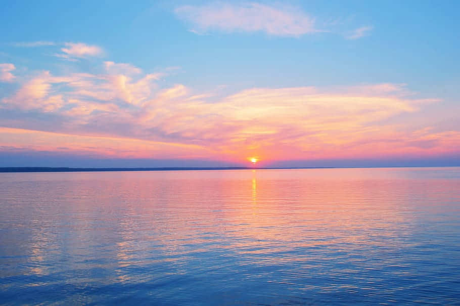 Pastel Beach 桌布 壁紙 — 夕陽將天空染成柔和的粉紅色和橙色，平靜的湖面倒映著閃爍的地平線。