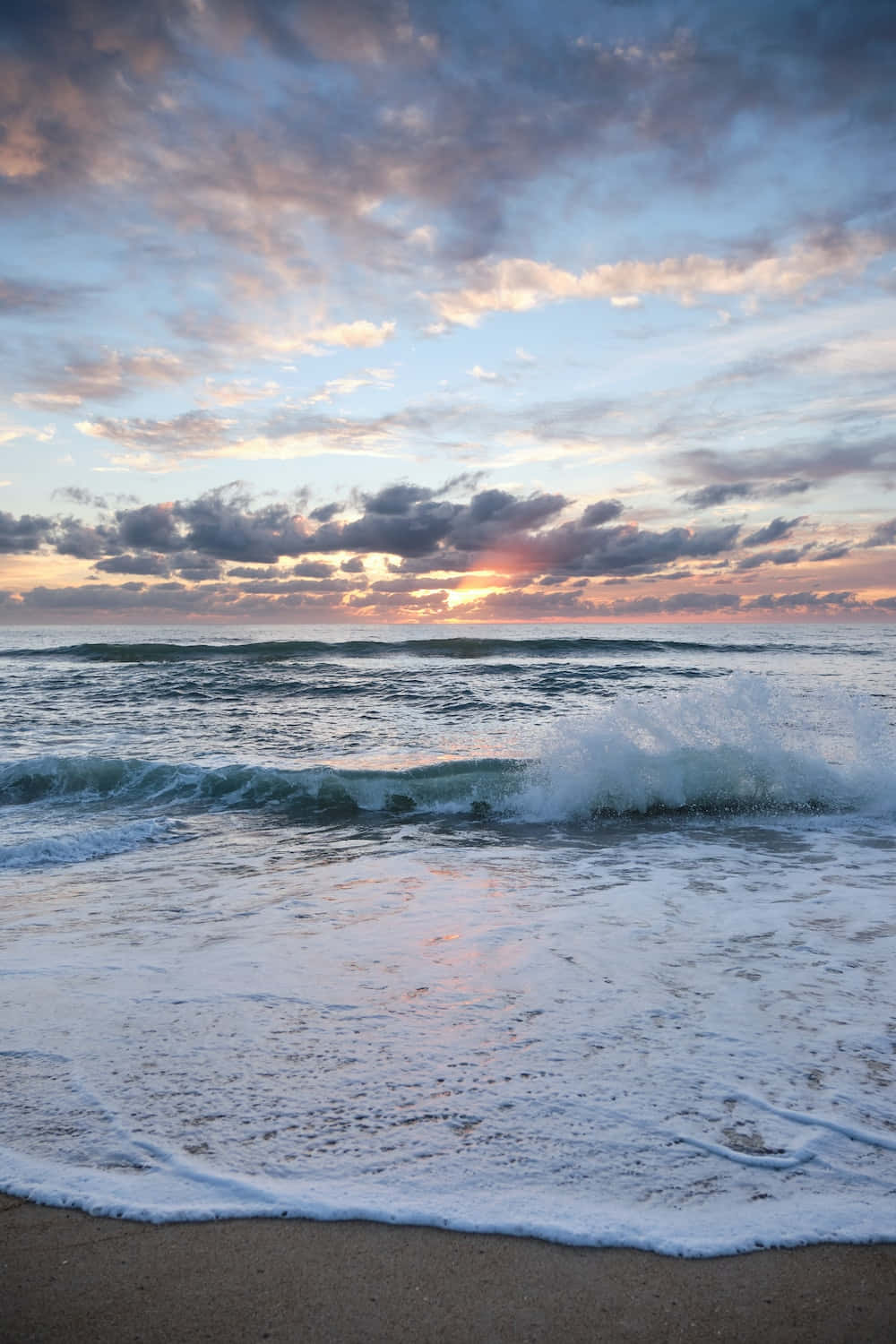 Sea Aesthetic 桌布 壁紙 — 夕陽將天空染成柔和的粉紅色和紫色，海浪拍打著沙灘。