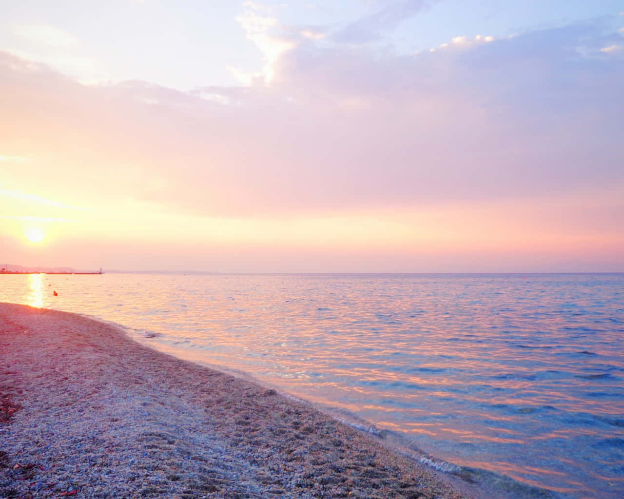 Pastel Beach 桌布 壁紙 — 夕陽將天空染成柔和的粉紅色和金色，溫柔的海浪拍打著卵石海灘。