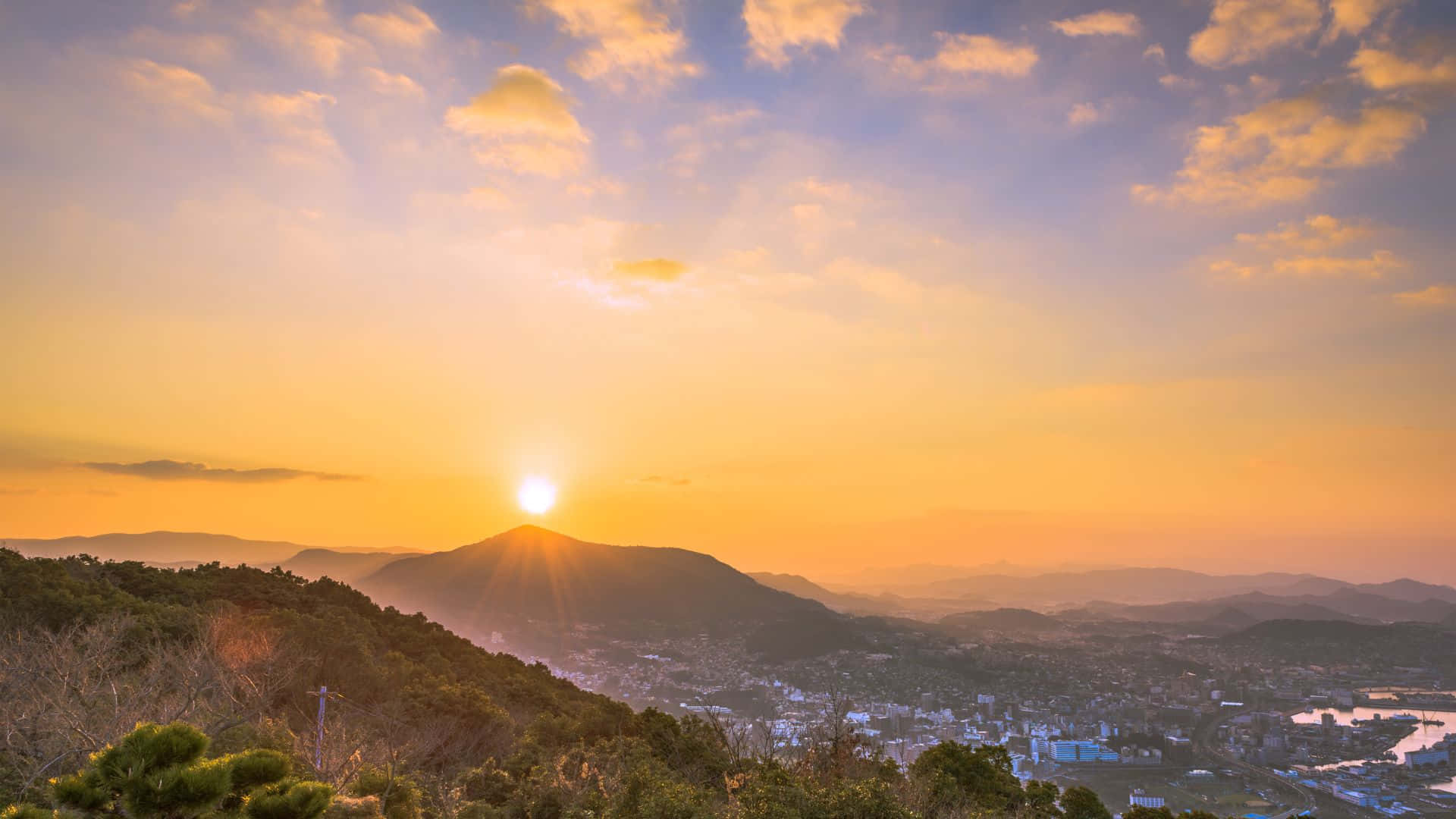 日出 桌布 壁紙 — 夕陽將天空染成橙色，光線從山後噴射而出，照耀山谷小鎮。