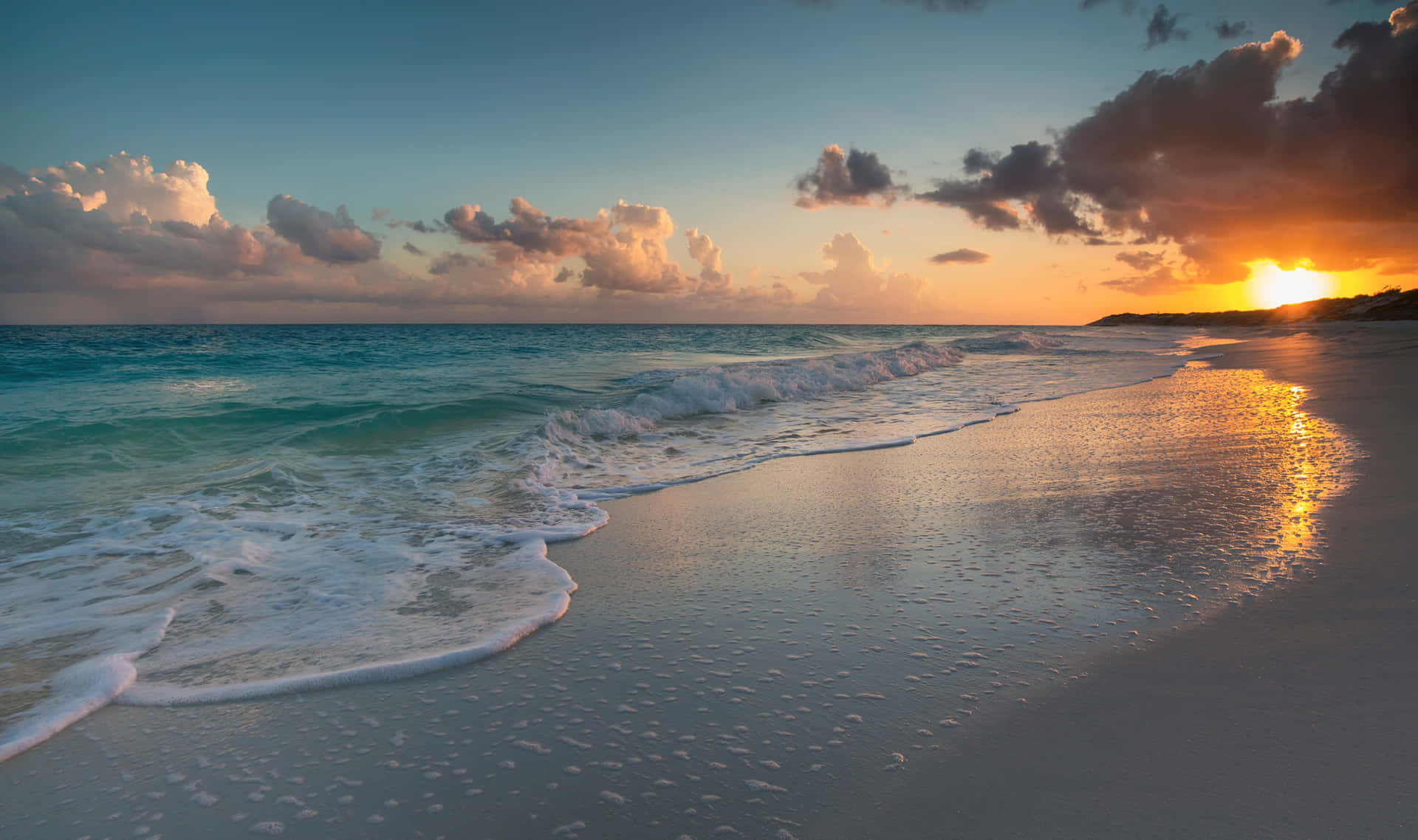 Beach Sunset HD 桌布 壁紙 — 夕陽將天空染成橙色和粉紅色，海浪拍打濕漉漉的沙灘，上空有零星雲朵。