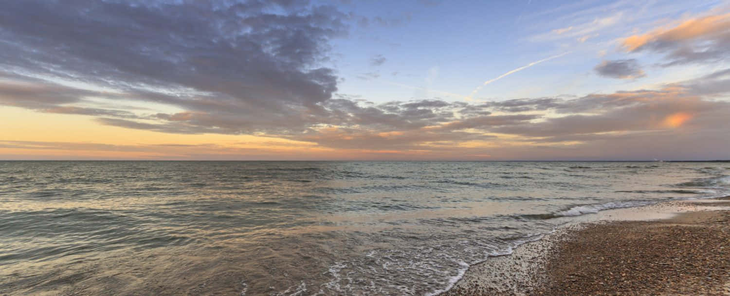 Lake Erie 桌布 壁紙 — 夕陽將天空染成溫暖的橙色和紫色，溫柔的海浪拍打著卵石海灘。