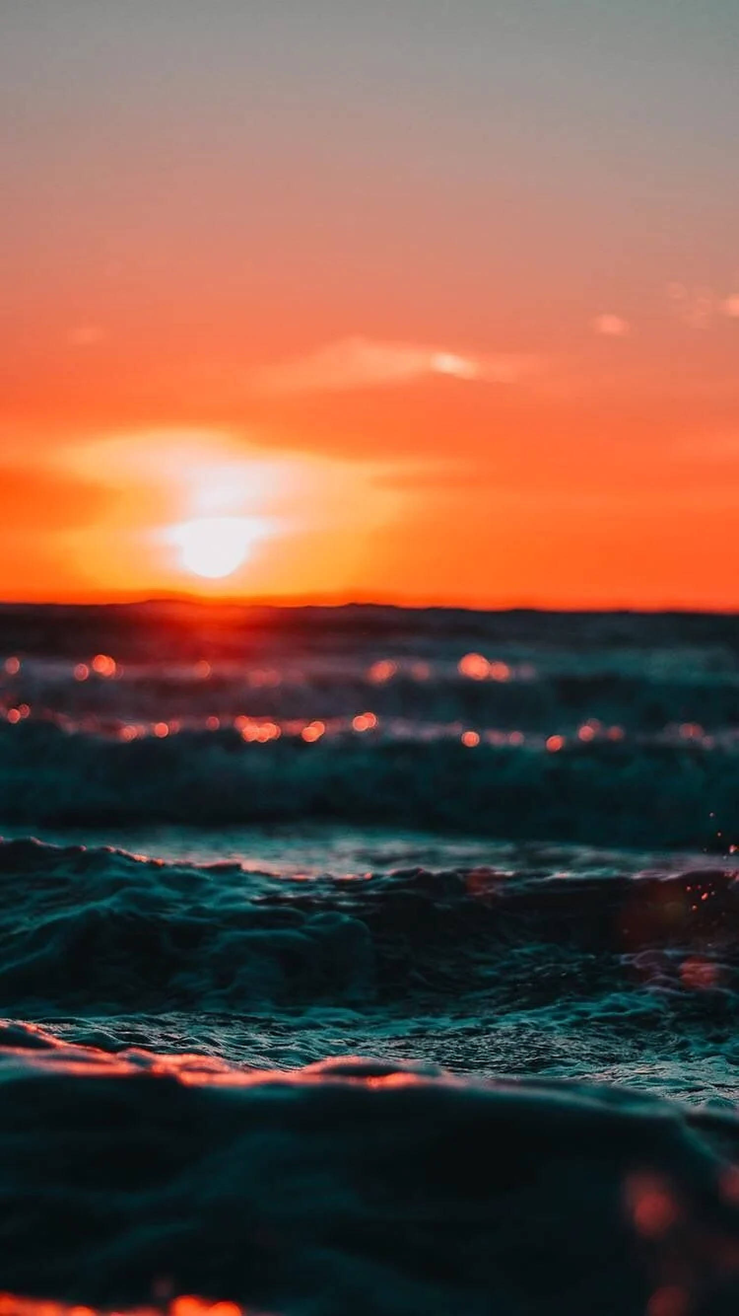 夕陽天空 桌布 壁紙 — 夕陽將天空染成火橙色，海浪拍打，帶有藍綠色亮點，映襯模糊的地平線。
