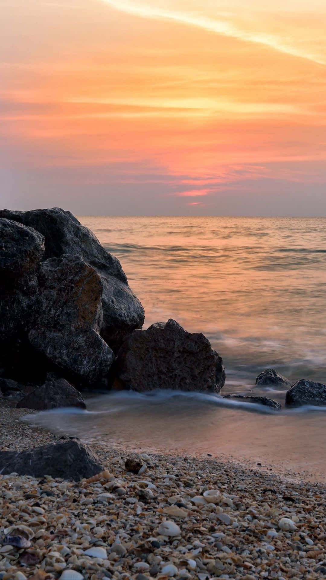 Coast 桌布 壁紙 — 夕陽將天空染成火橙色，溫柔的海浪拍打著卵石海灘上的暗色岩石。