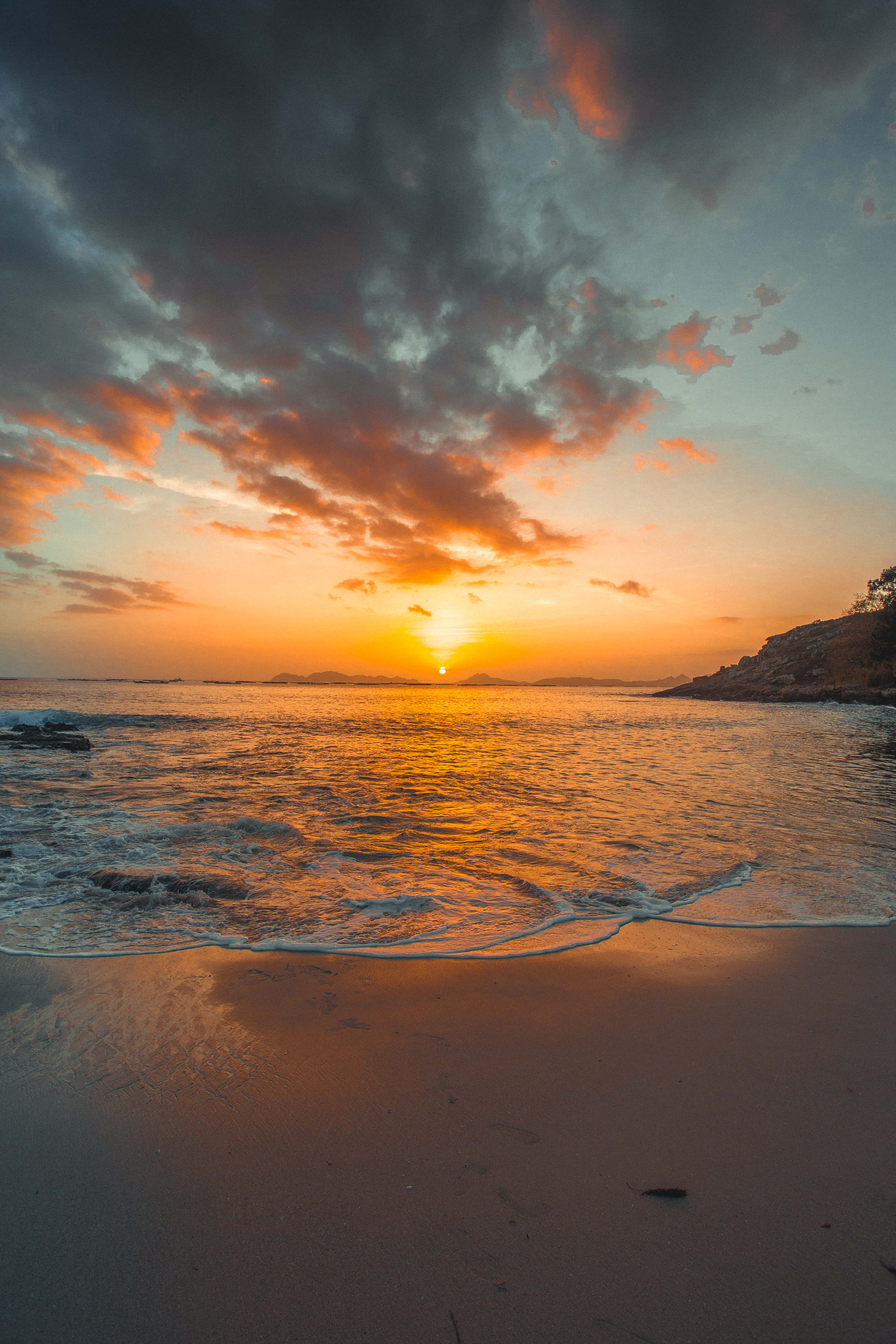 Beach Sunset HD 桌布 壁紙 — 夕陽將天空染成火橙色和深灰色的雲朵，海浪輕輕拍打著沙灘。