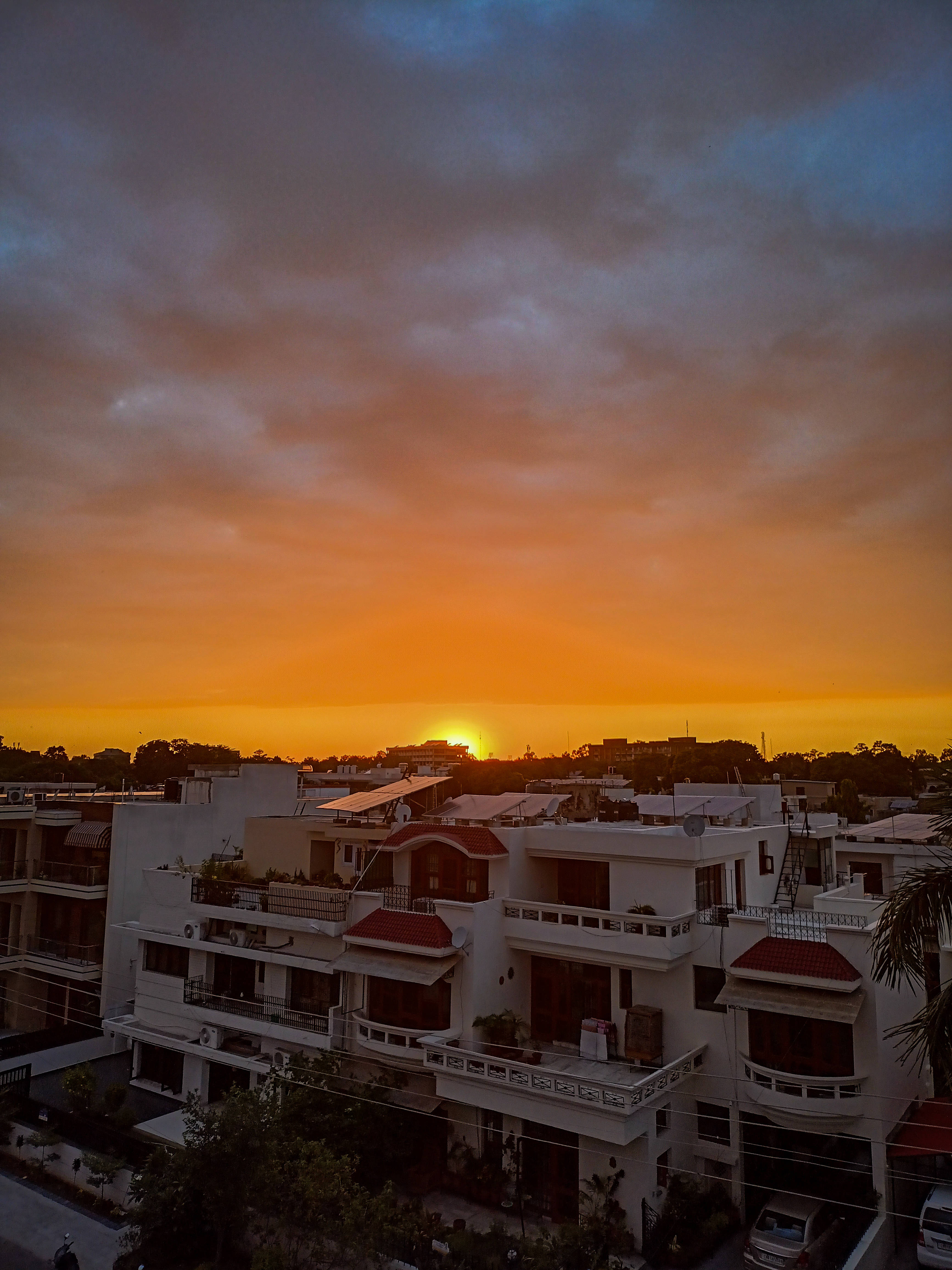 Indian 桌布 壁紙 — 夕陽將天空染成火橙色和深藍色，映照在白色住宅建築和紅色屋頂之上。