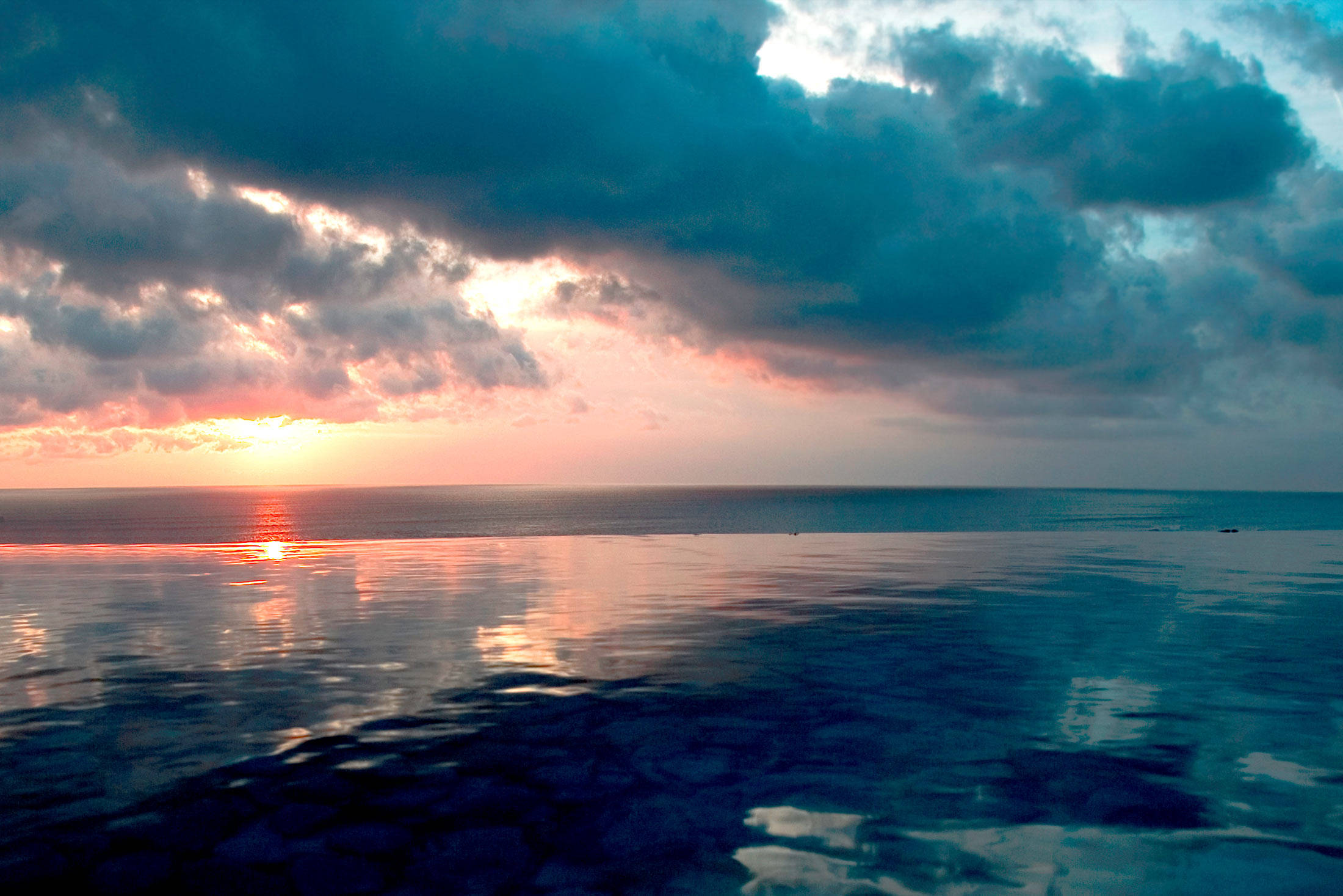 印尼 桌布 壁紙 — 夕陽將天空染成火橙色和深青色的雲彩，映照在平靜的海面上。