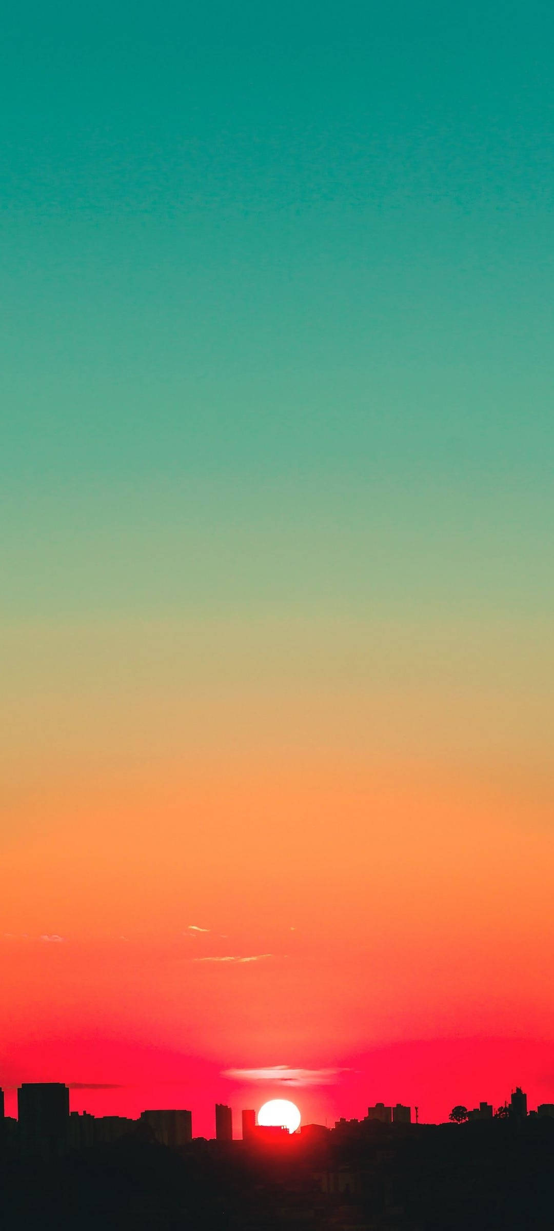 夕陽天空 桌布 壁紙 — 夕陽將天空染成火橙色和藍綠色，城市天際線的輪廓在夕陽下顯得格外鮮明。