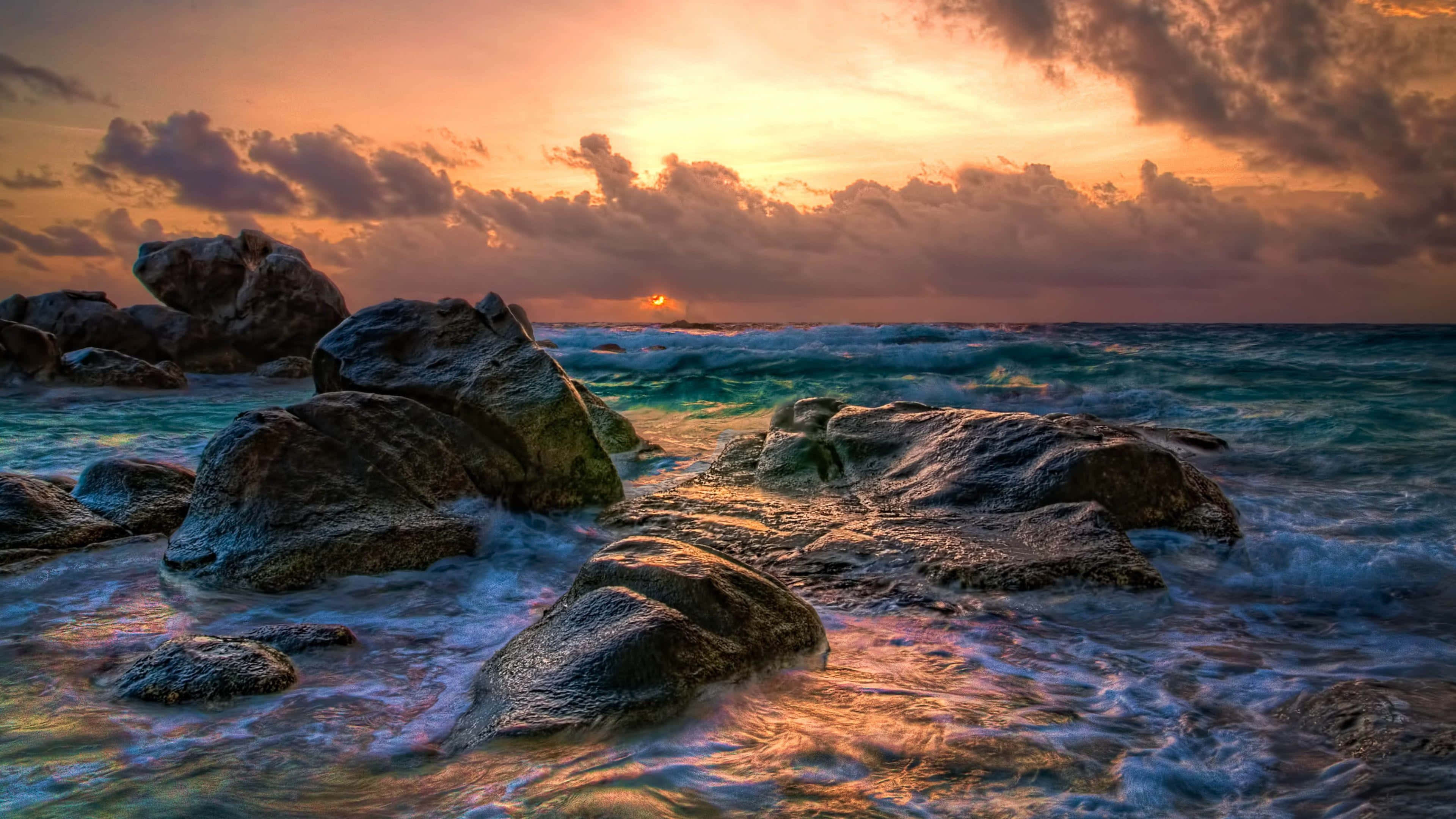 3840x2160 動態圖片 桌布 壁紙 — 夕陽將天空染成火熱的橙色，海浪拍打著崎嶇的海岸岩石。