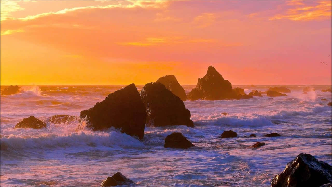 海洋 桌布 壁紙 — 夕陽將天空染成火熱的橙色，海浪拍打著崎嶇海岸線上的黑色火山岩。
