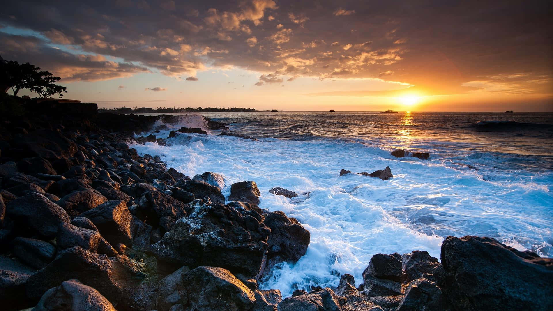 夏威夷 桌布 壁紙 — 夕陽將天空染成火熱的橙色，海浪拍打著崎嶇海岸線上的黑色火山岩。