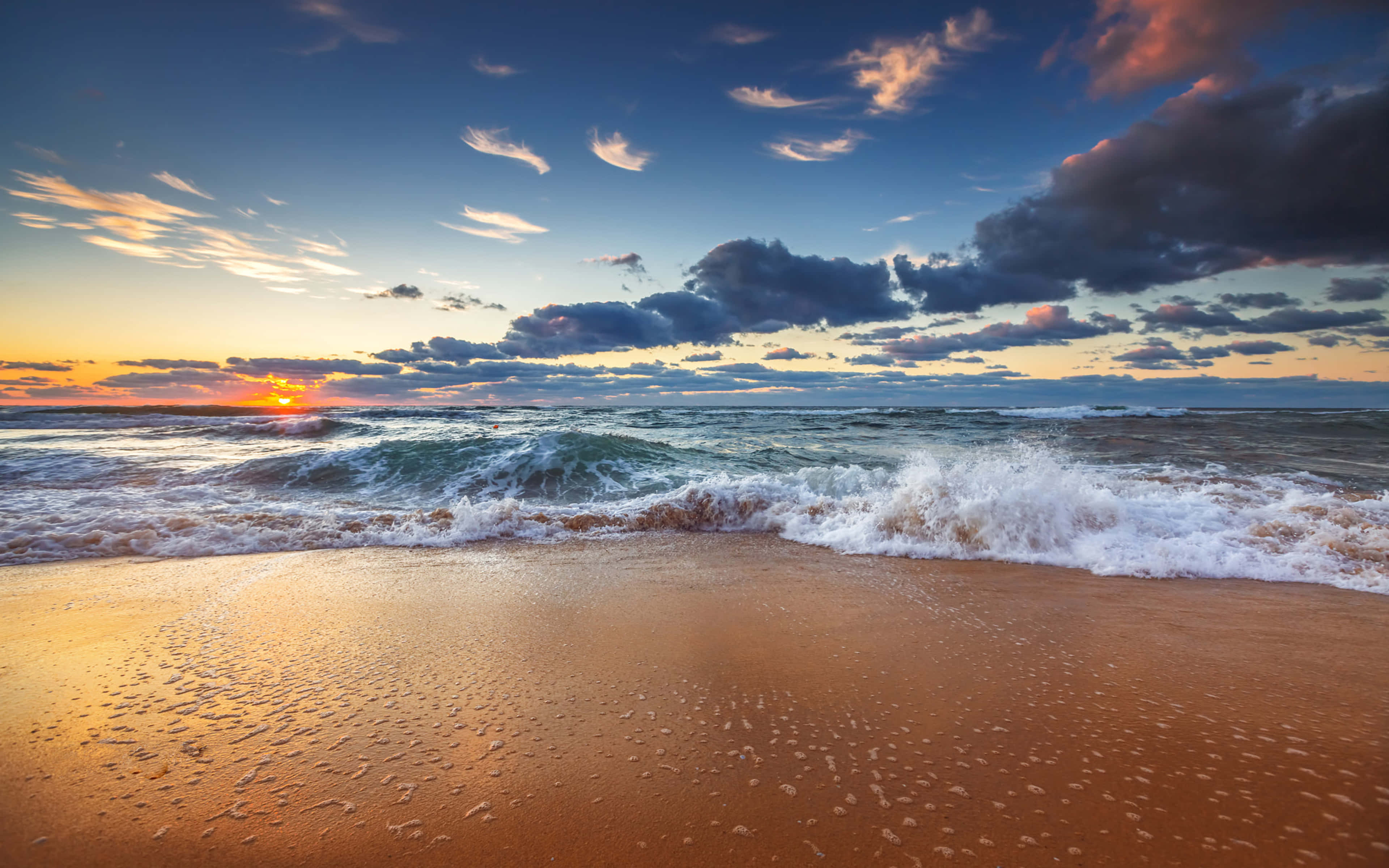 Weather 桌布 壁紙 — 夕陽將天空染成火熱的橙色和深藍色，海浪拍打著濕漉漉的金色沙灘。