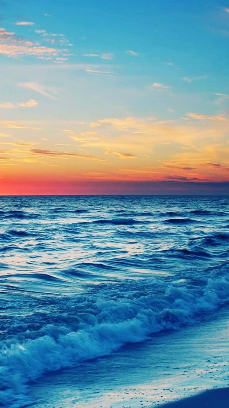 Sunset Beach iPhone 桌布 壁紙 — 夕陽將天空染成火熱的橙色和粉紅色，映照在平靜的海洋上，溫柔的海浪拍打著沙灘。
