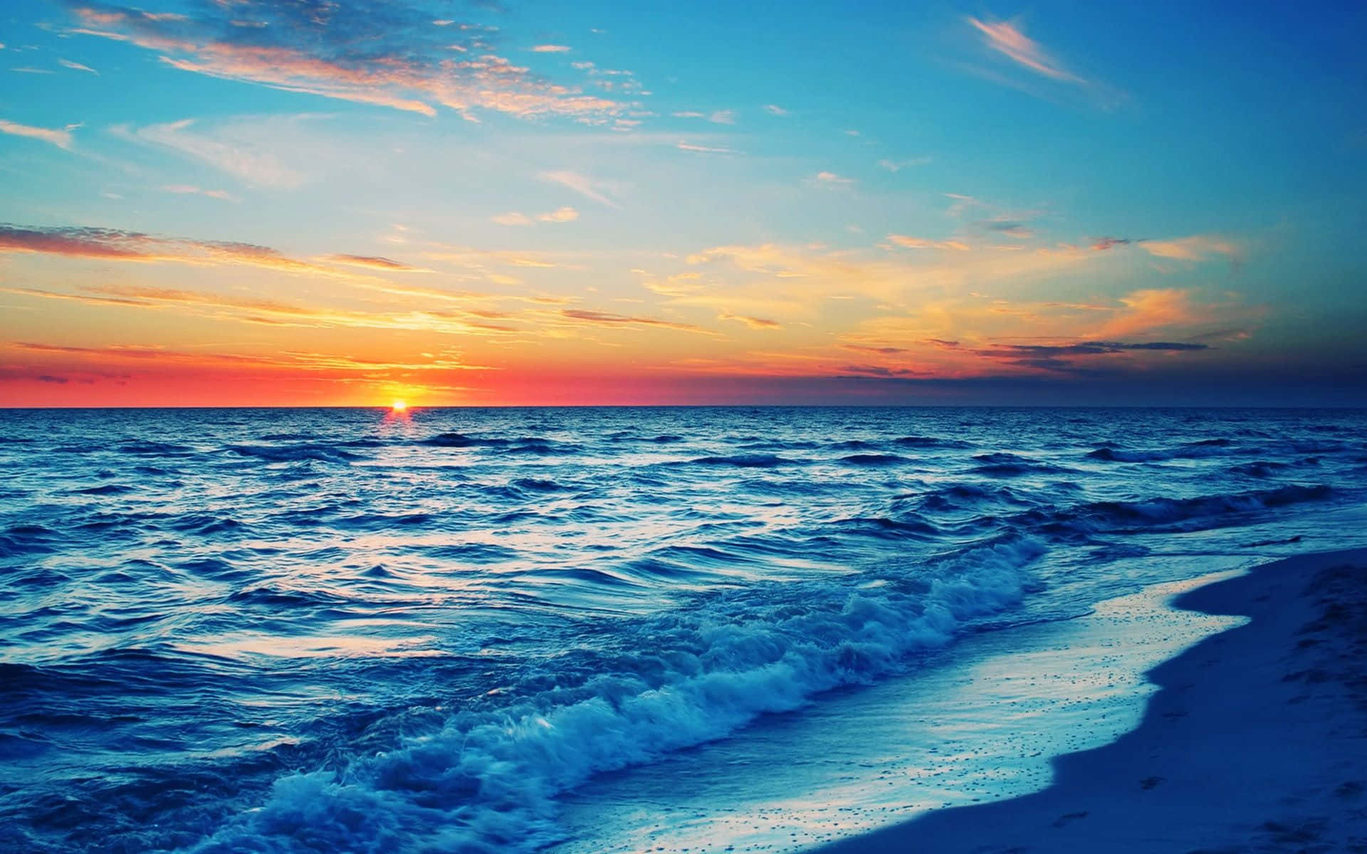 Beautiful Beach 桌布 壁紙 — 夕陽將天空染成火熱的橙色和粉紅色，海浪在廣闊的藍天下拍打著沙灘。