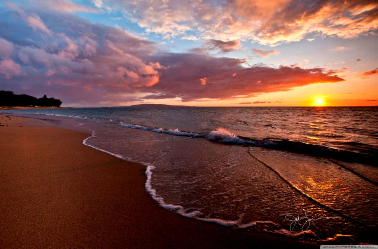 Beach Sunset HD 桌布 壁紙 — 夕陽將天空染成火熱的橙色和粉紅色，海浪輕輕拍打沙灘。
