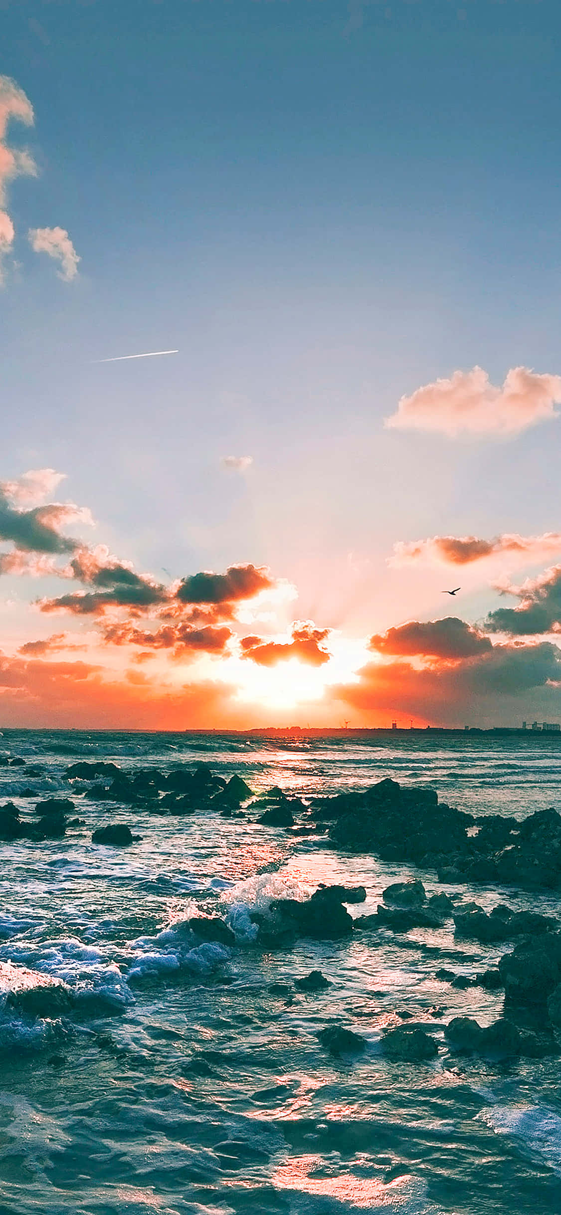 Clouds Aesthetics 桌布 壁紙 — 夕陽將天空染成火熱的橙色和粉紅色，海浪拍打著海岸線上的暗色岩石。