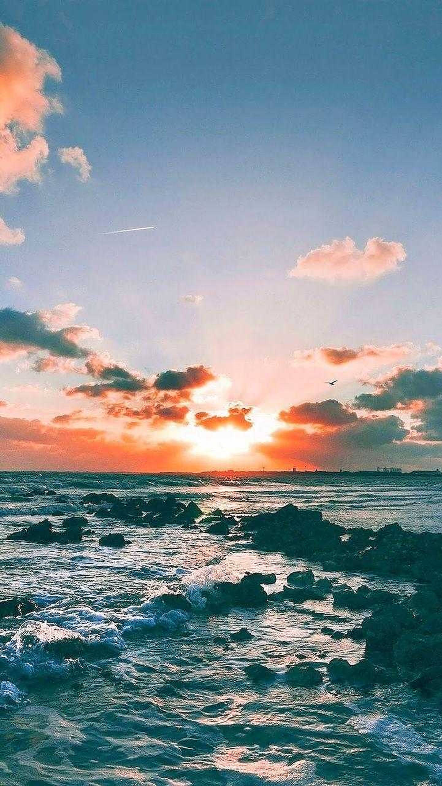 日落 桌布 壁紙 — 夕陽將天空染成火熱的橙色和粉紅色，海浪拍打著海岸邊的黑色岩石。