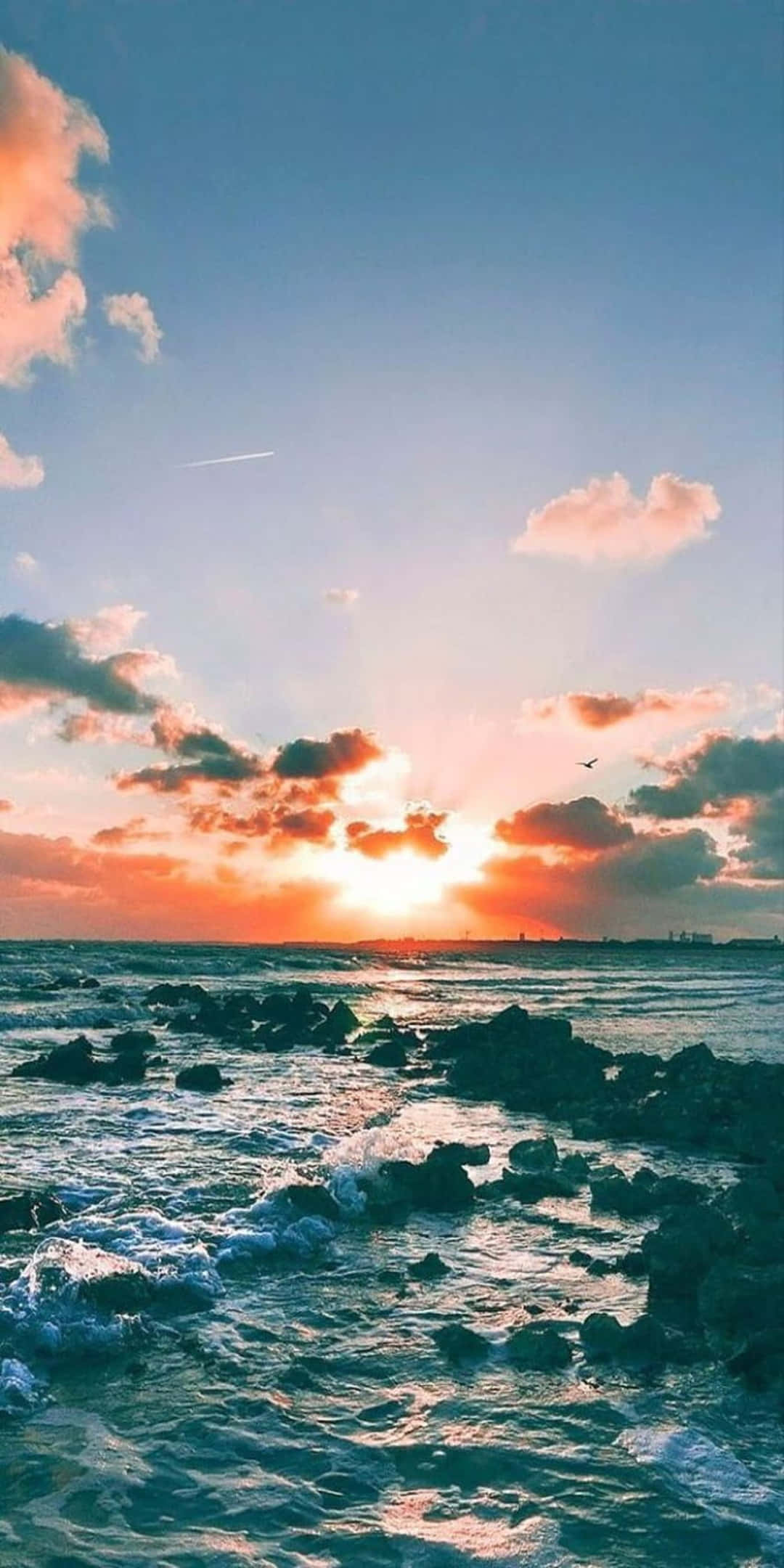 Pixel 3 Summer 桌布 壁紙 — 夕陽將天空染成火熱的橙色和粉紅色，海浪拍打著海岸線上的黑色岩石。
