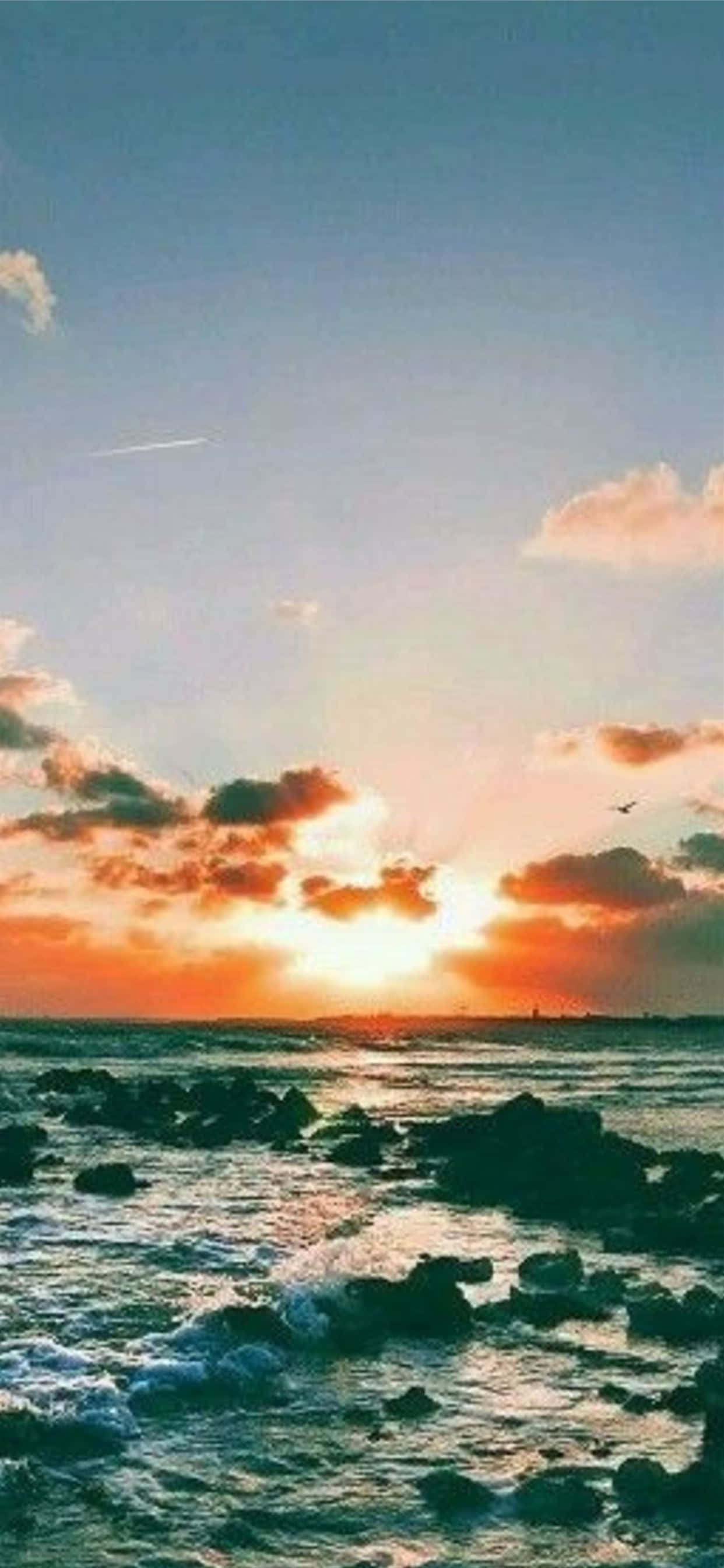 Sunset Aesthetic 桌布 壁紙 — 夕陽將天空染成火熱的橙色和粉紅色，海浪拍打著海岸線上的黑色岩石。