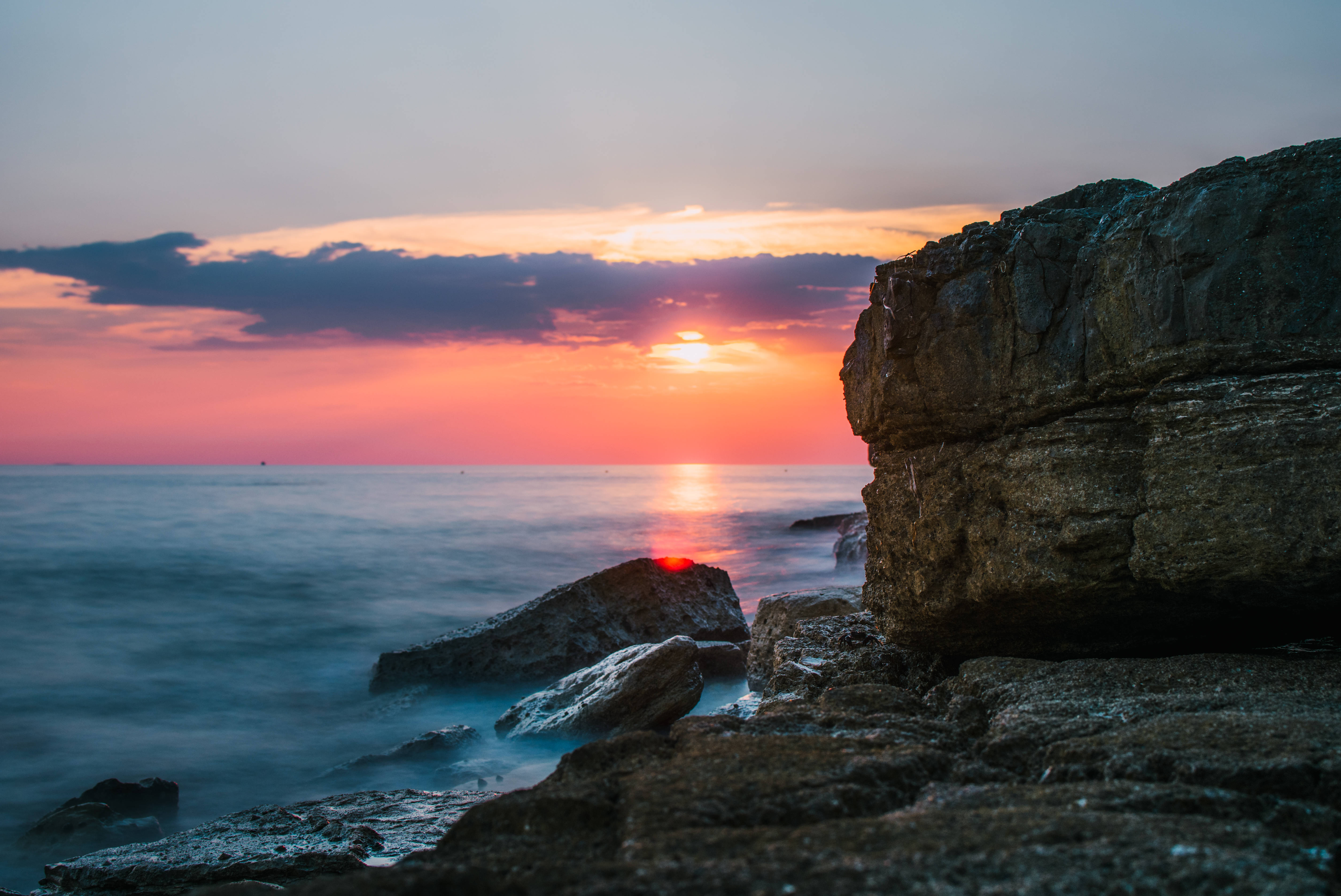 Croatia 桌布 壁紙 — 夕陽將天空染成火熱的橙色和粉紅色，海浪輕輕拍打崎嶇的海岸岩石。