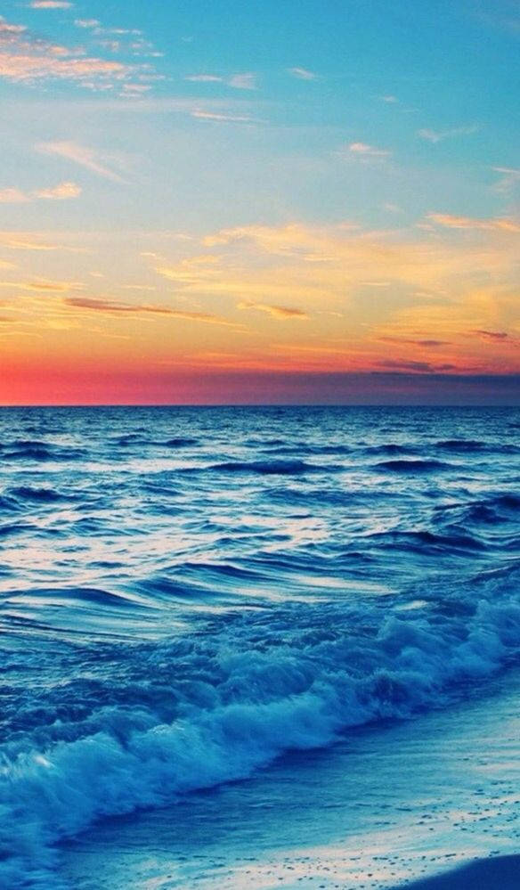 malibu iPhone 桌布 壁紙 — 夕陽將天空染成火熱的橙色和粉紅色，映照在廣闊的海洋上，溫柔的海浪拍打著沙灘。