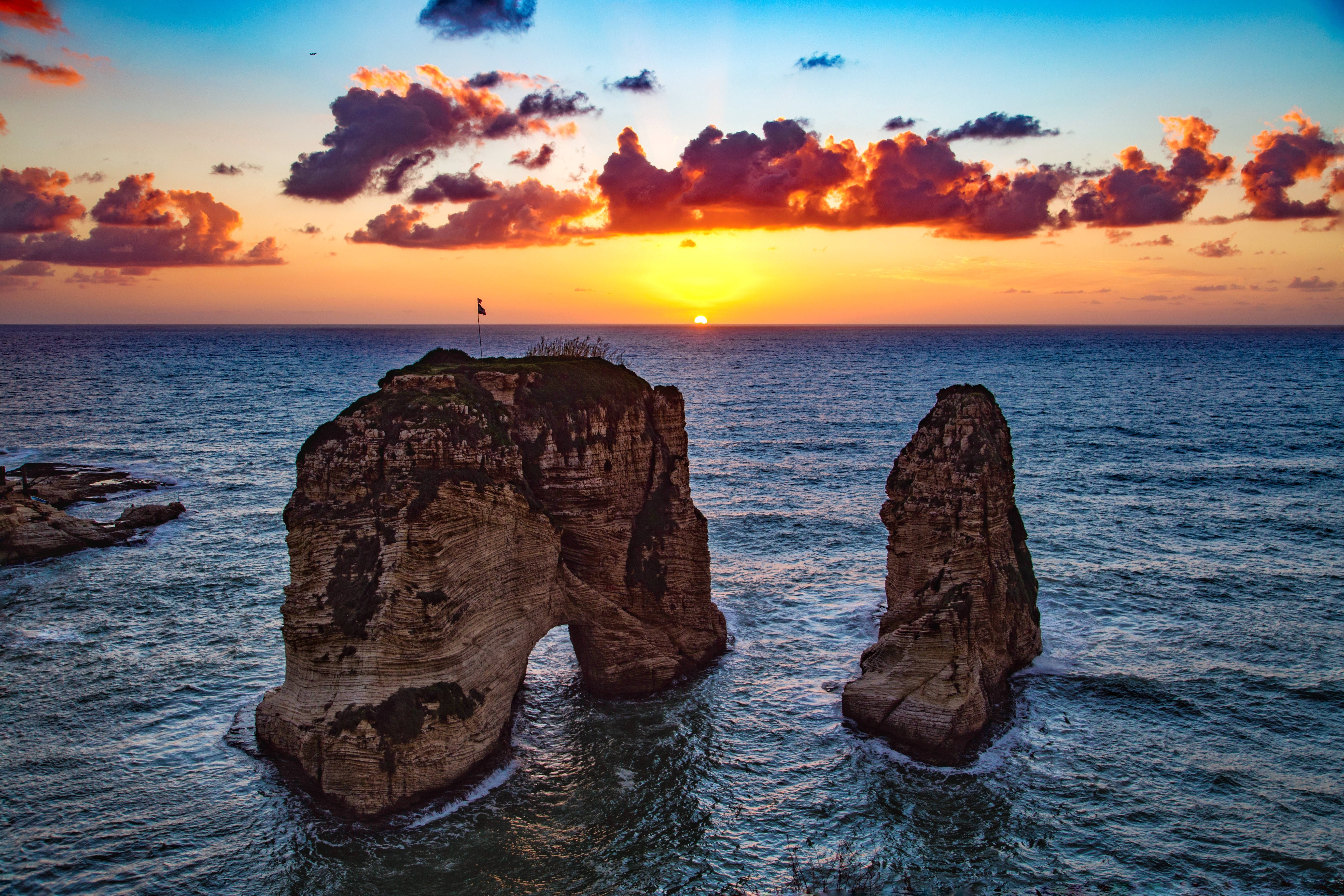 Lebanon 桌布 壁紙 — 夕陽將天空染成火熱的橙色和紫色，海浪拍打著兩座高聳的海蝕柱。