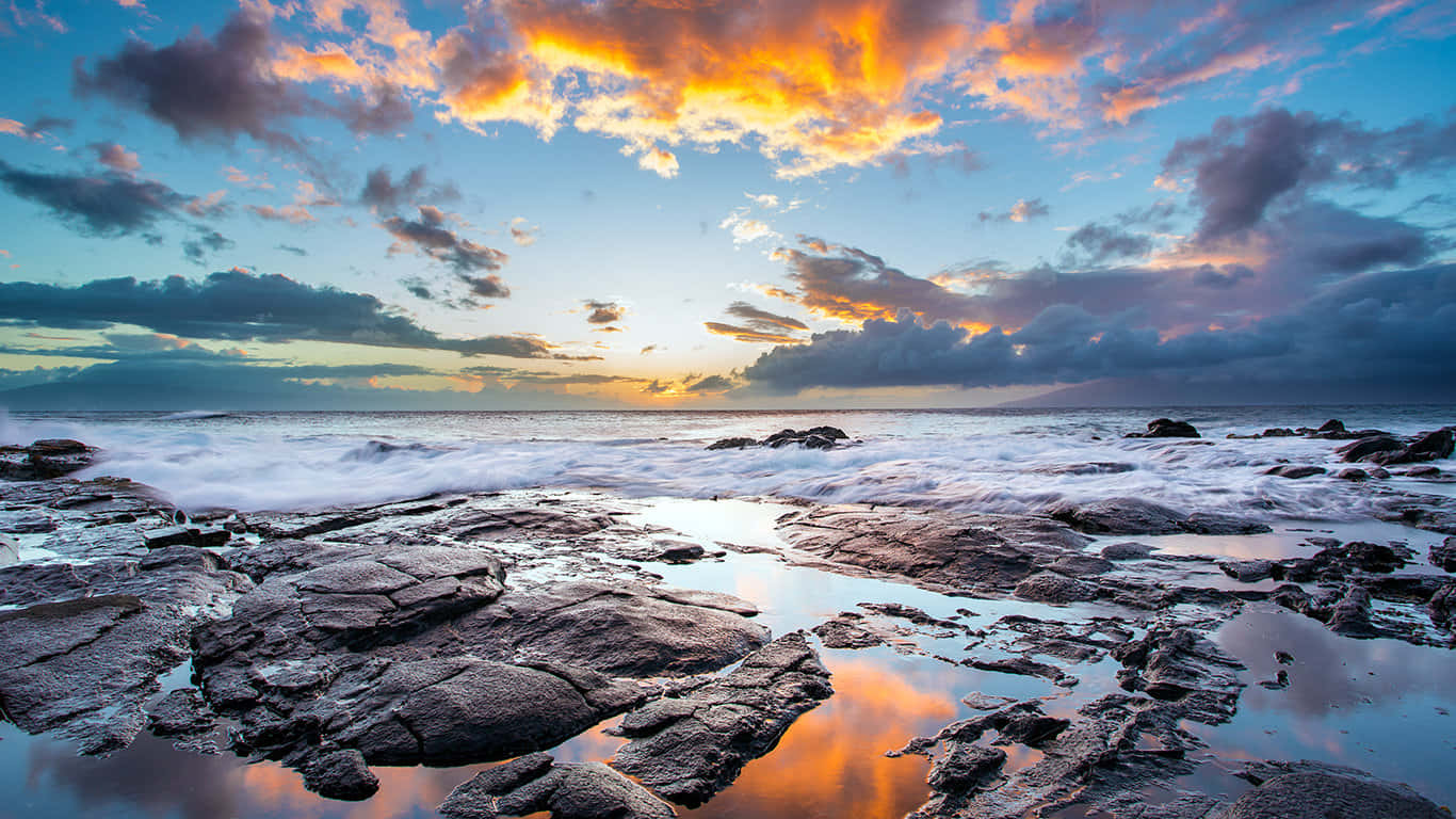 Sea 桌布 壁紙 — 夕陽將天空染成火熱的橙色和紫色，海浪拍打崎嶇的海岸岩石，映照出鮮豔的雲彩。