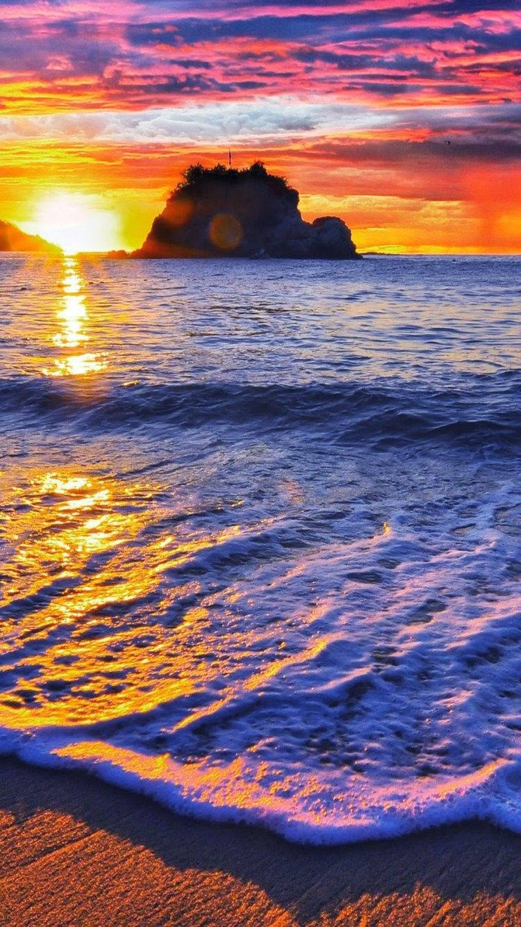 波多黎各 桌布 壁紙 — 夕陽將天空染成火熱的橙色和紫色，海浪拍打沙灘，遠處有岩石島的輪廓。