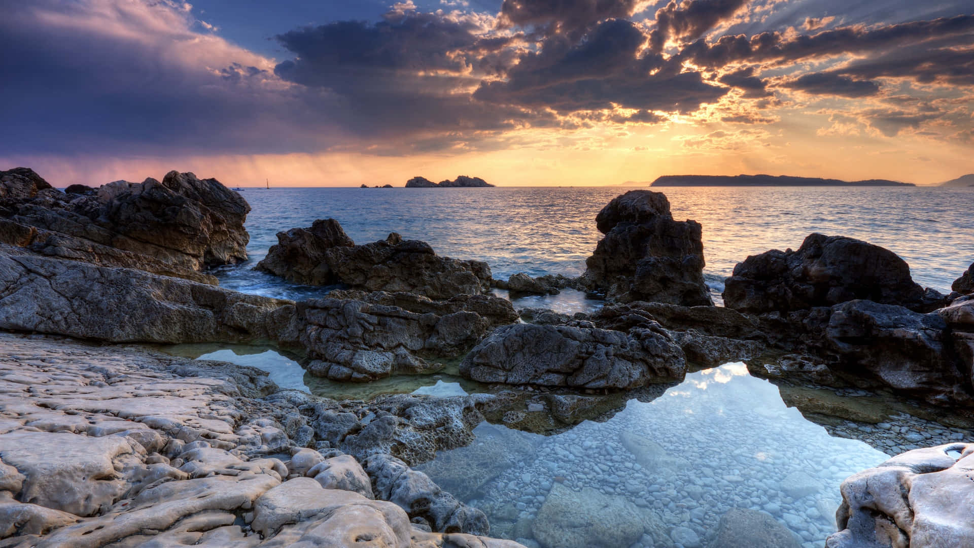 rocky 桌布 壁紙 — 夕陽將天空染成火熱的橙色和紫色，海浪拍打著堅固的海岸岩石。