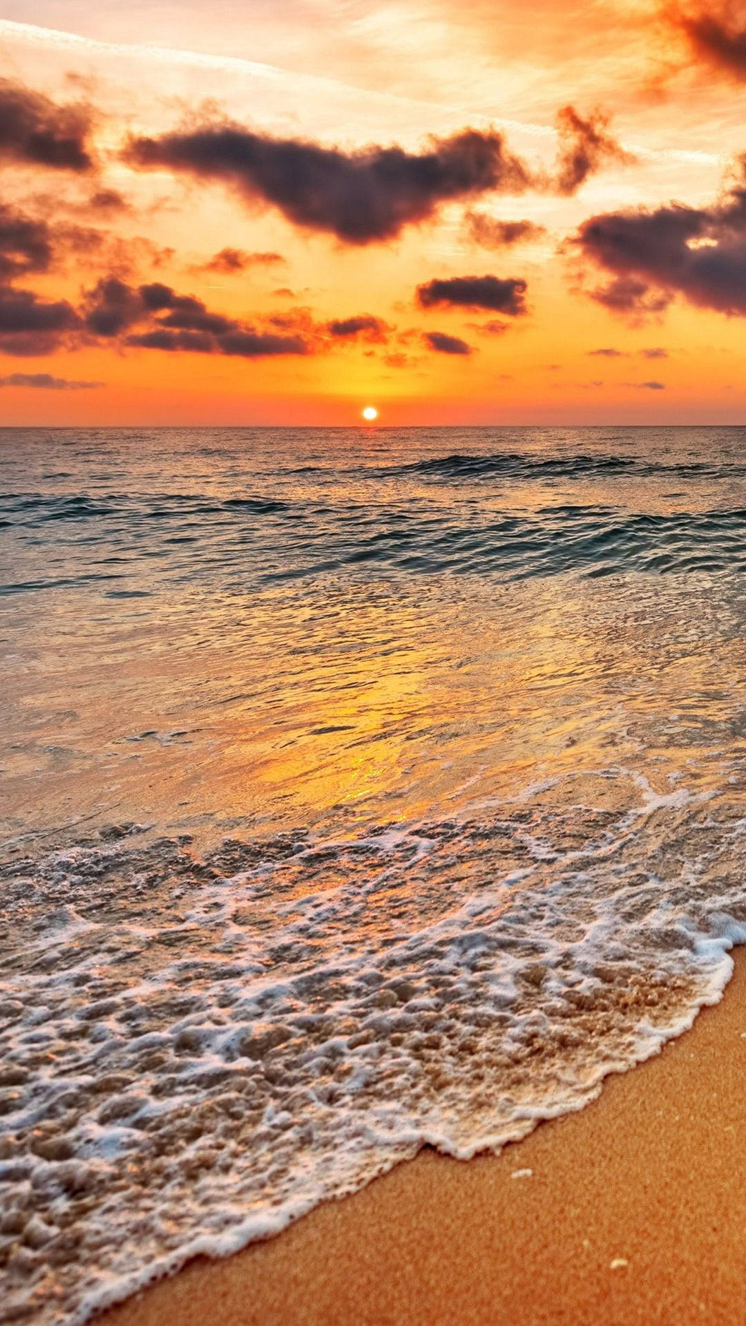 Sunset iPhone 桌布 壁紙 — 夕陽將天空染成火熱的橙色和紫色，海浪輕輕拍打著金色的沙灘。