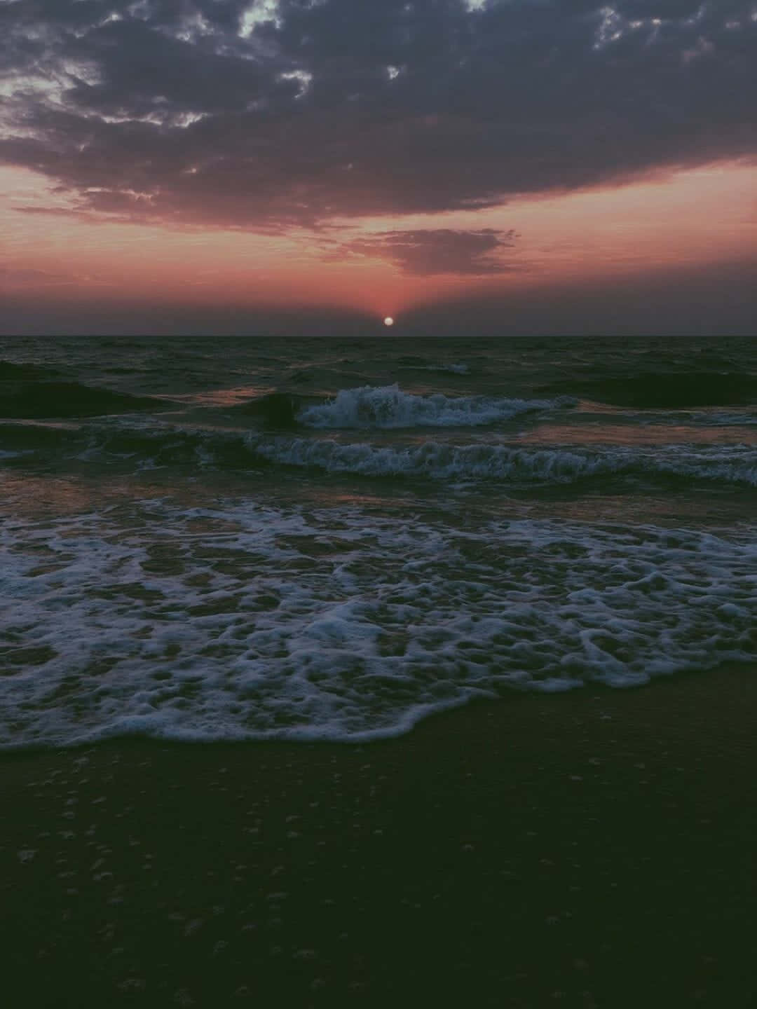 Tumblr Photography 桌布 壁紙 — 夕陽將天空染成火熱的橙色和紫色，海浪拍打著深色沙灘。
