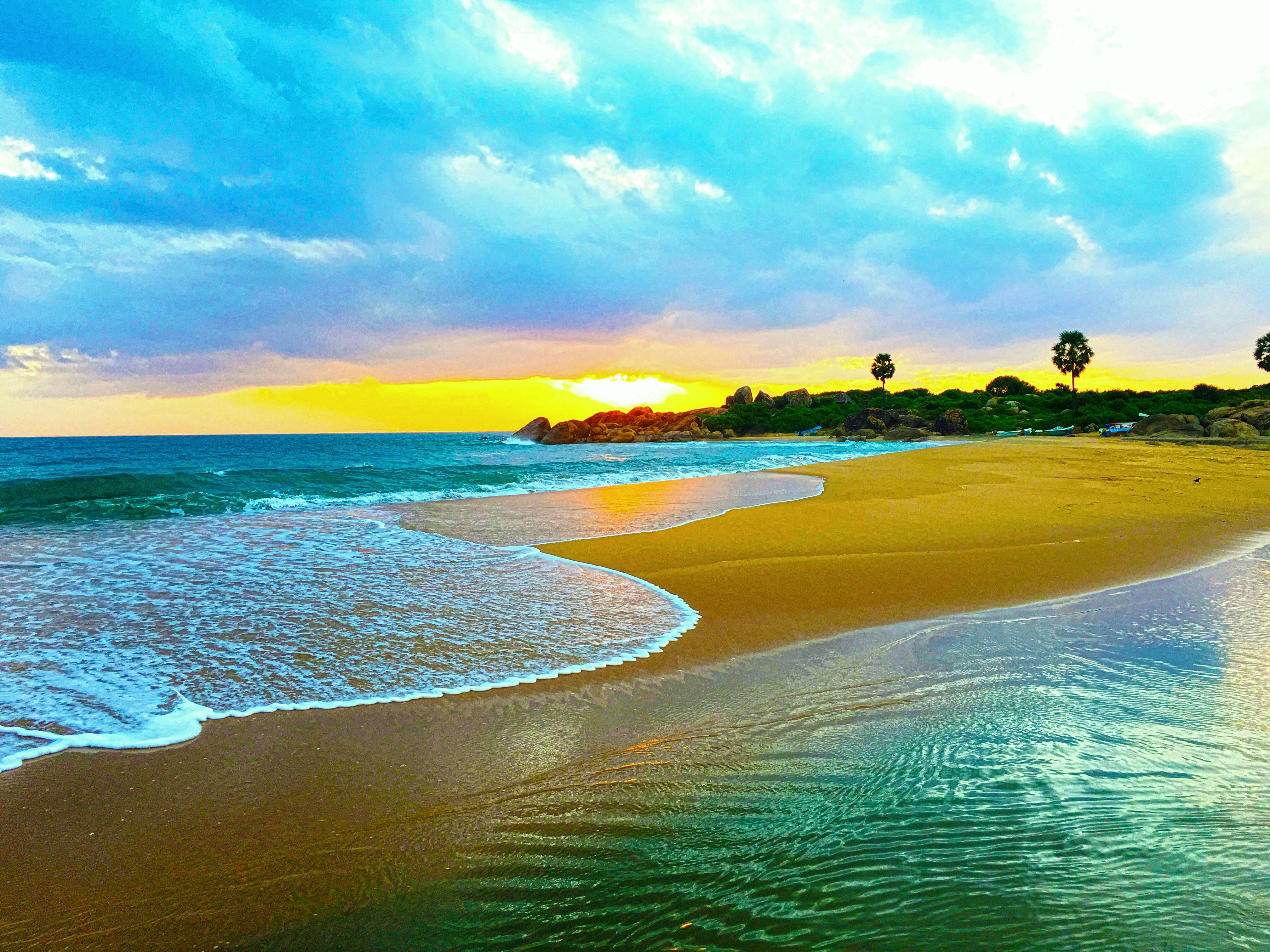 Sri Lanka 桌布 壁紙 — 夕陽將天空染成火熱的橙色和藍色，海浪輕輕拍打著棕櫚樹成排的金色沙灘。