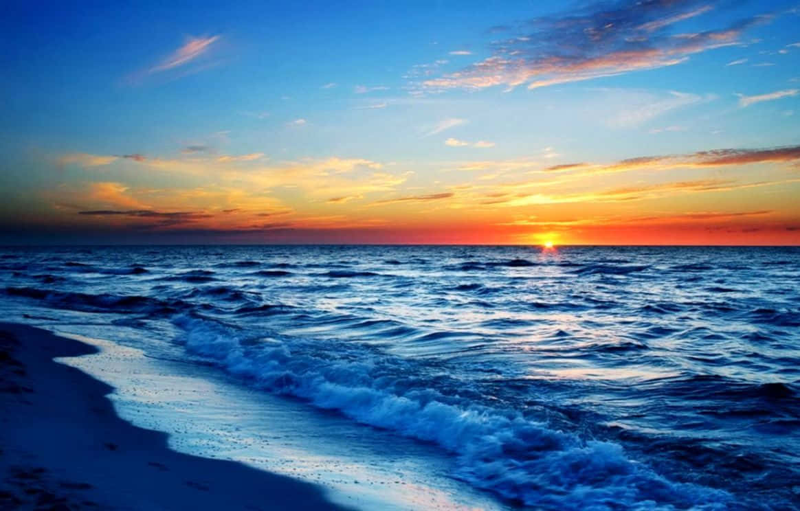 Best Summer 桌布 壁紙 — 夕陽將天空染成火熱的橙色和藍色，海浪拍打著沙灘。