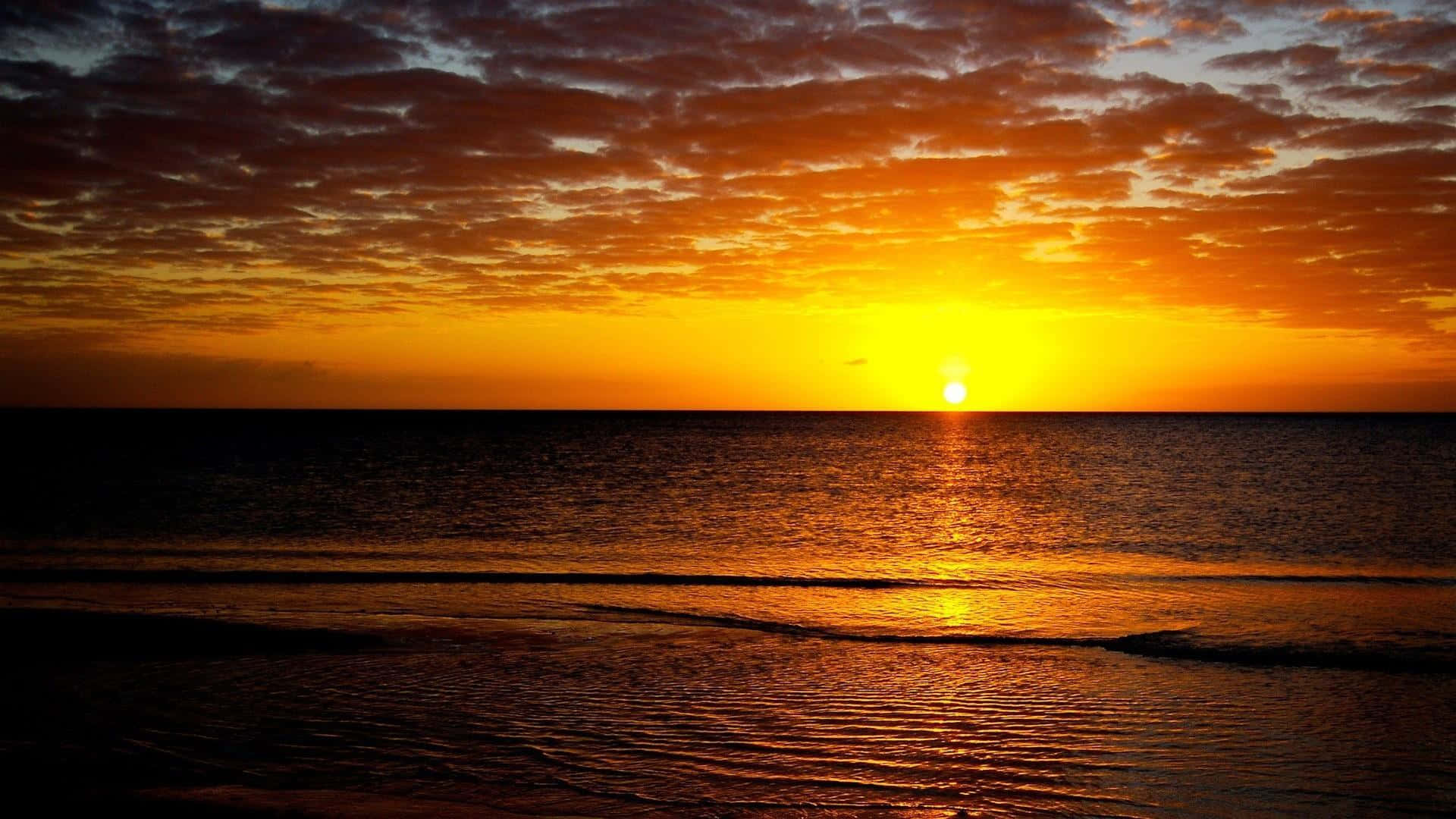 桌布 壁紙 — 夕陽將天空染成火紅的橙色和金色，太陽在平靜的海洋上沉入地平線。