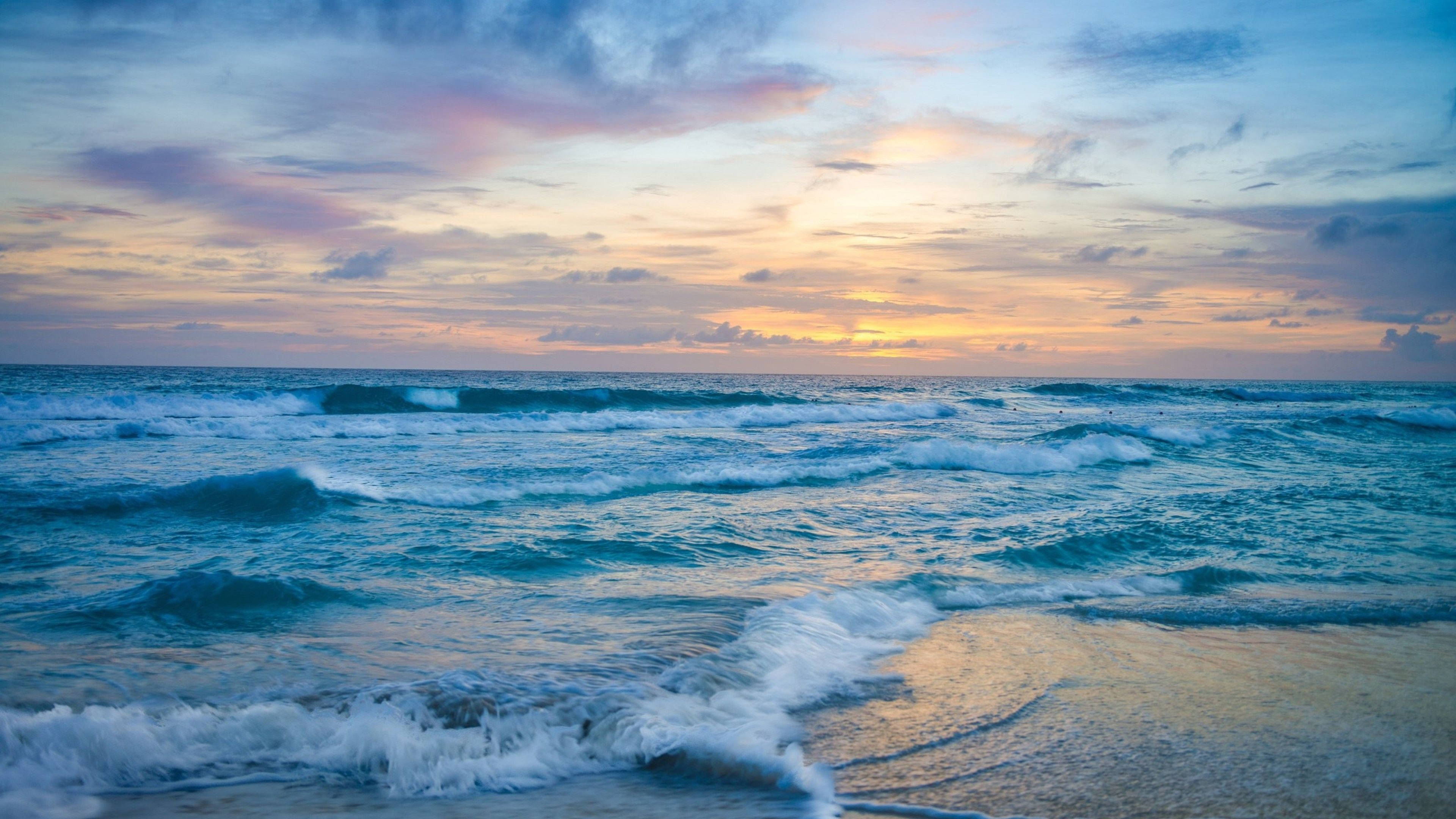 海洋 桌布 壁紙 — 夕陽將天空染成粉紅、金色和藍色，海浪拍打沙灘。