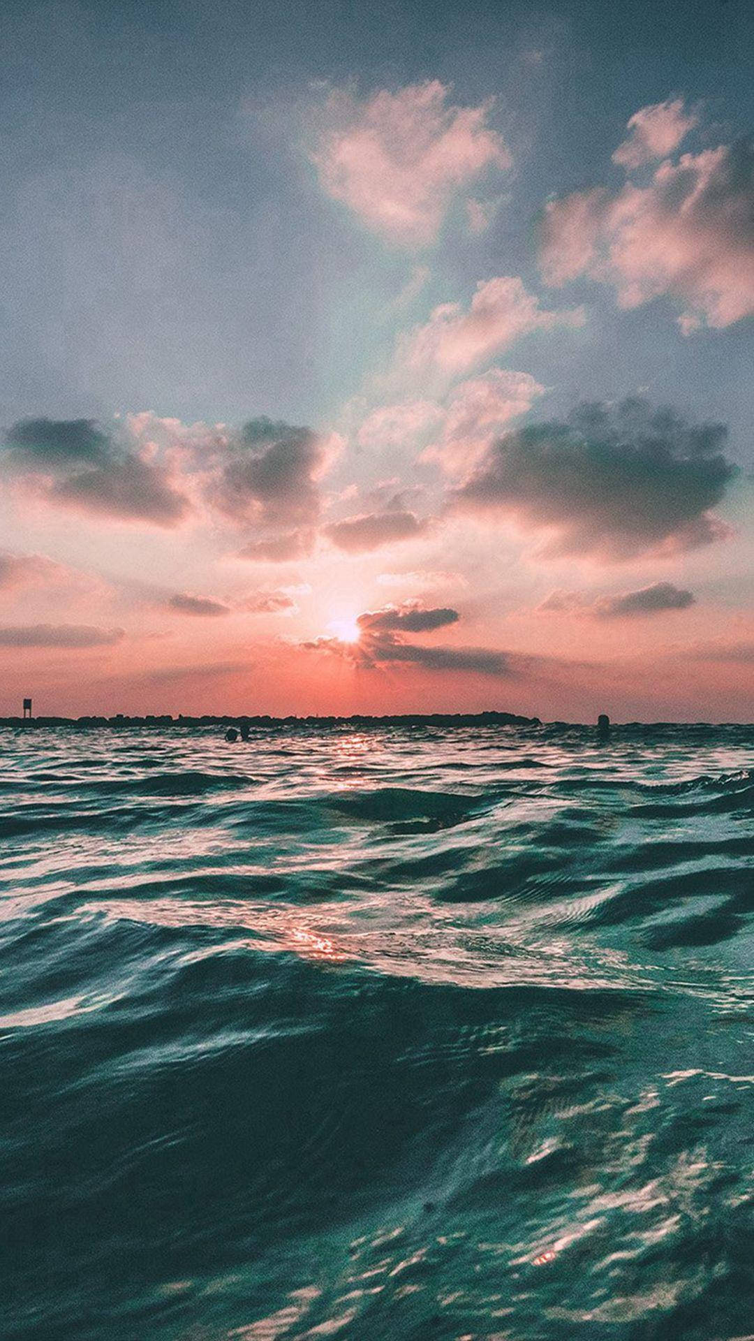 海洋 桌布 壁紙 — 夕陽將天空染成粉紅色和橙色，倒映在質感豐富的藍綠色海浪上。