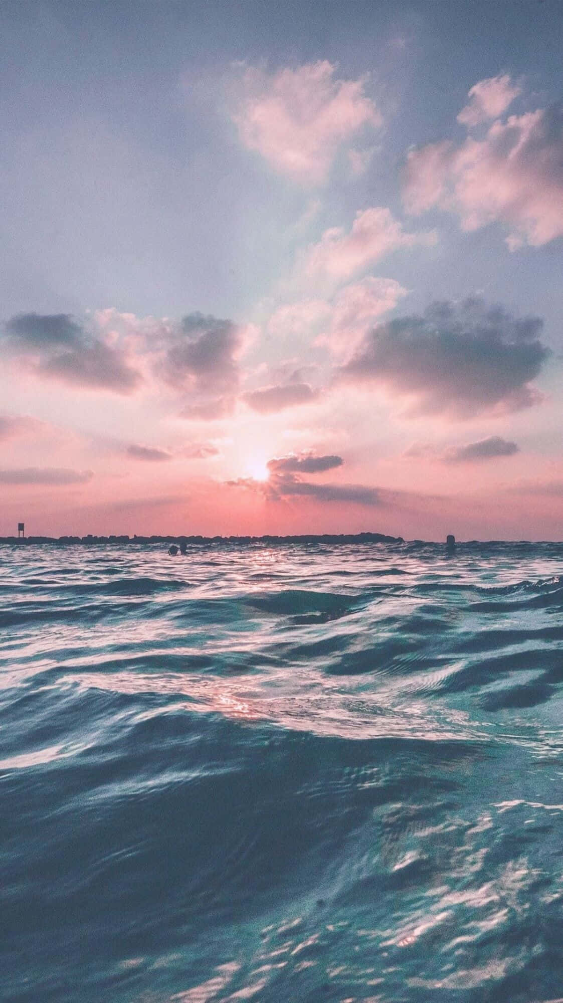 海洋 桌布 壁紙 — 夕陽將天空染成粉紅色和紫色，海浪在碧綠的海水上泛起漣漪。