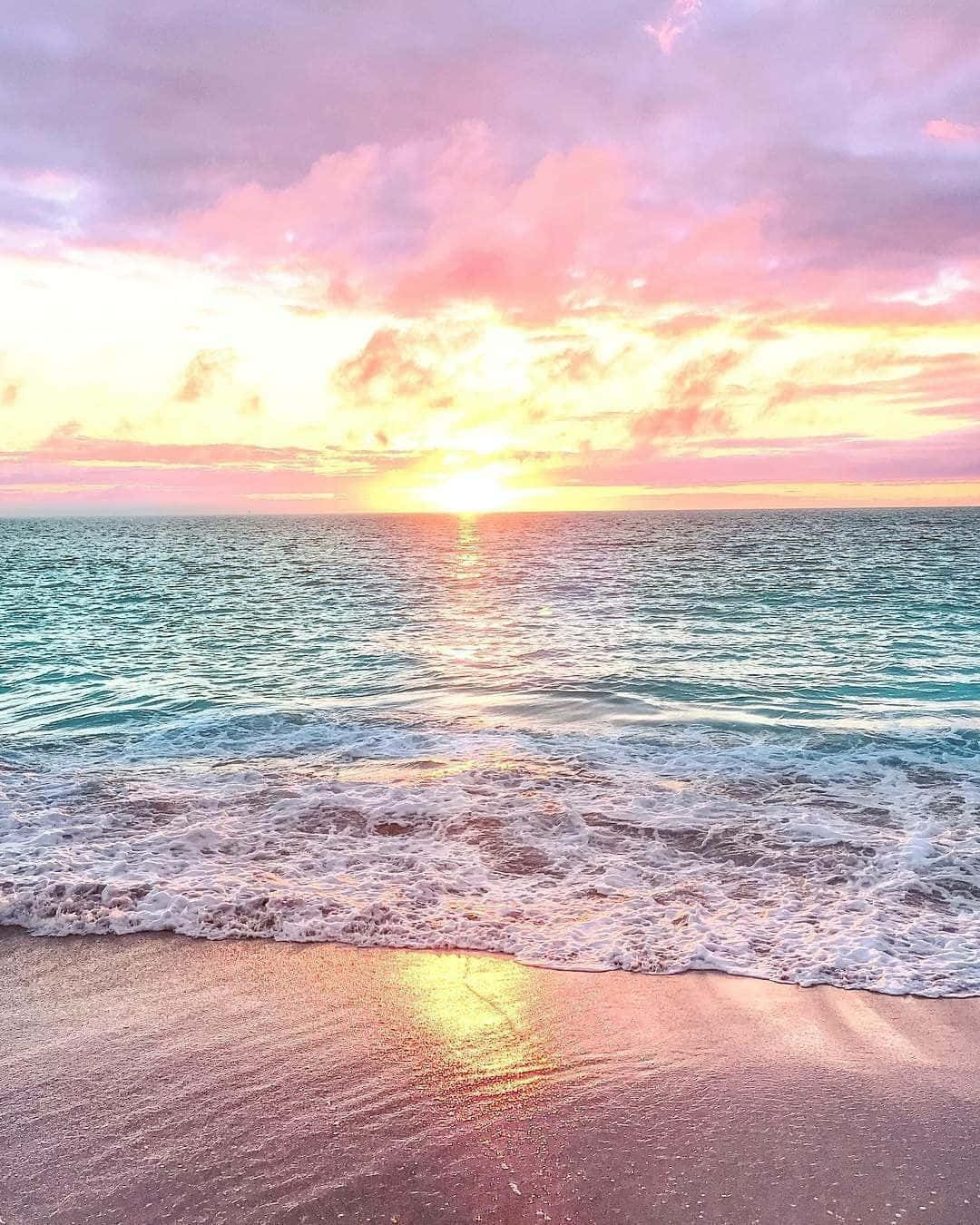 Pastel Beach 桌布 壁紙 — 夕陽將天空染成粉紅色和金色，海浪輕輕拍打沙灘。