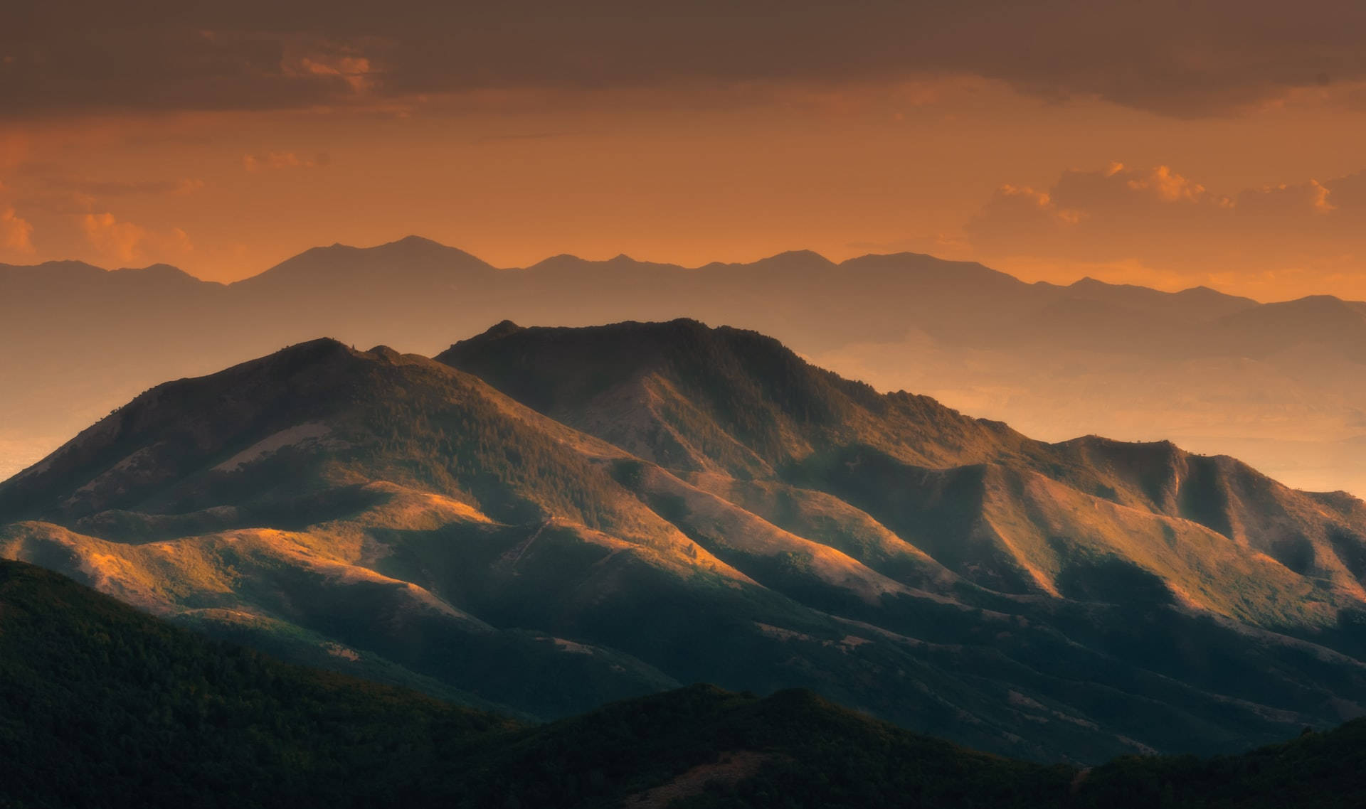 Mountain Landscape 桌布 壁紙 — 夕陽將層層疊疊的山脊沐浴在溫暖的橙色和深沉的陰影中，營造出寧靜而富有氣氛的景觀。